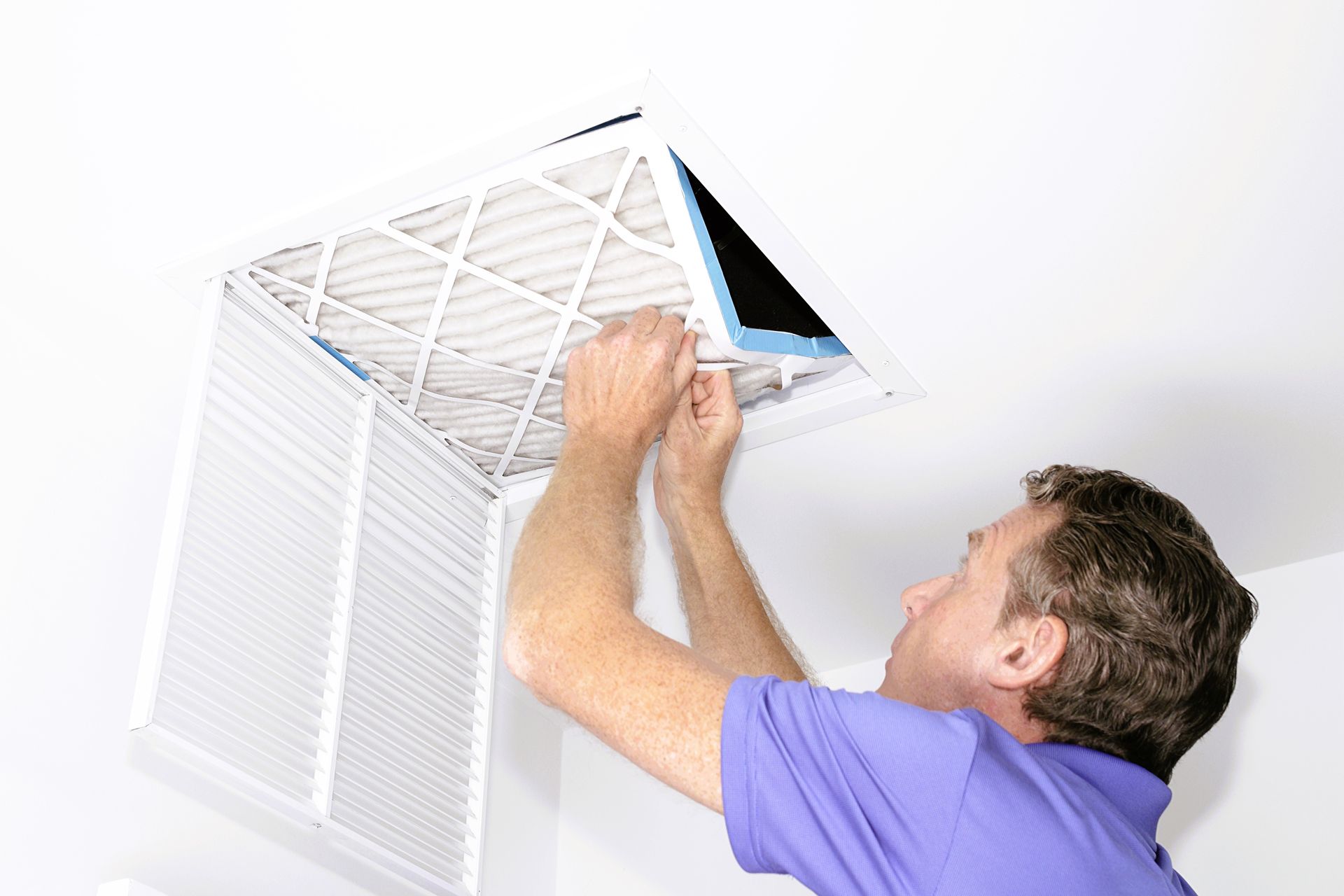 A man in a blue shirt is replacing an air filter in a ceiling vent