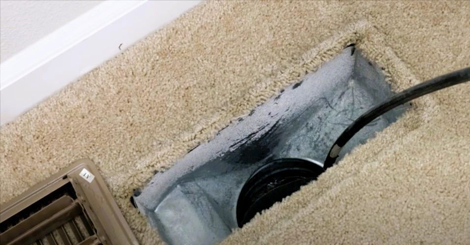 Exposed air vent and duct with a cable running through the carpet floor.