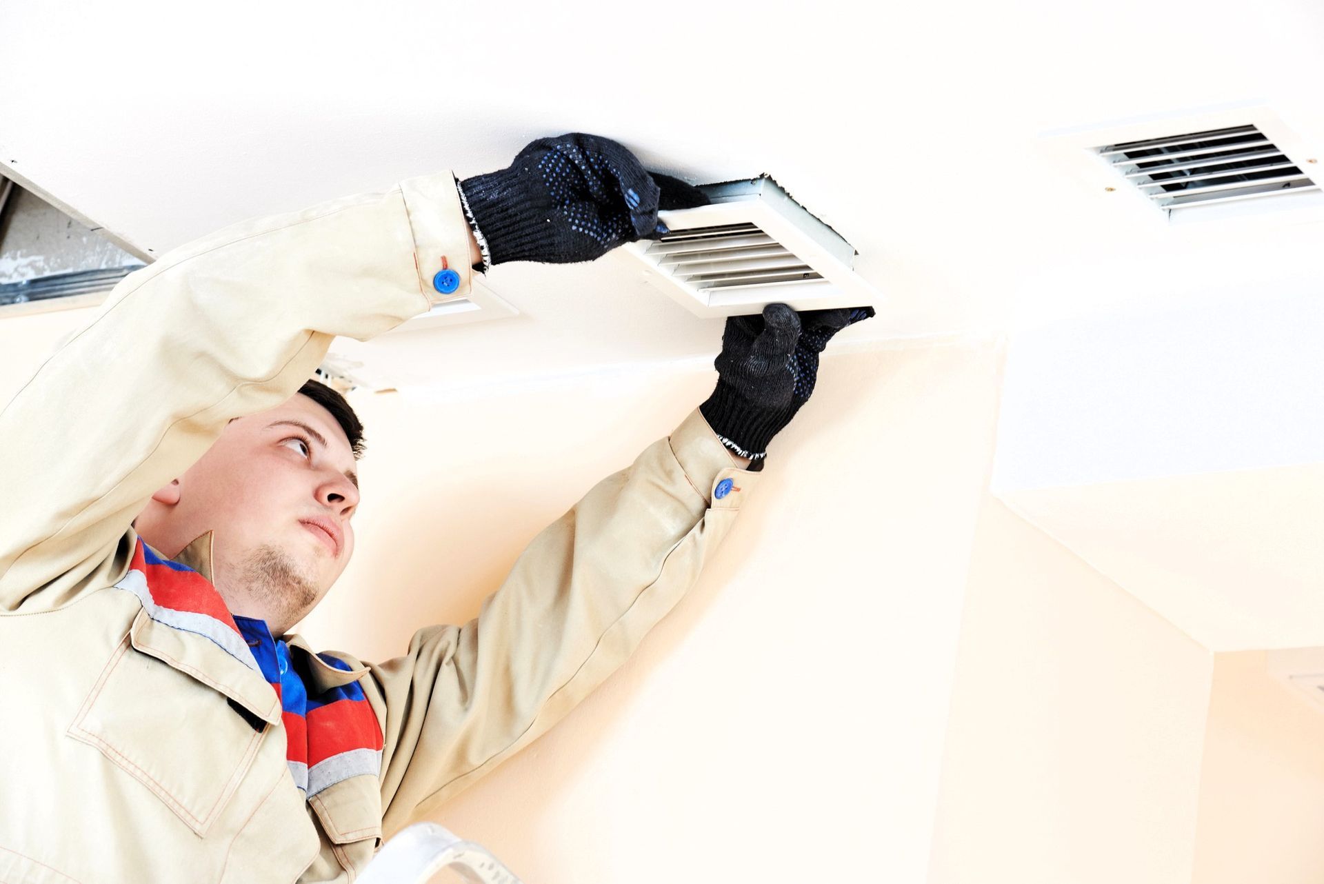 Person in gloves installing a ceiling air vent.