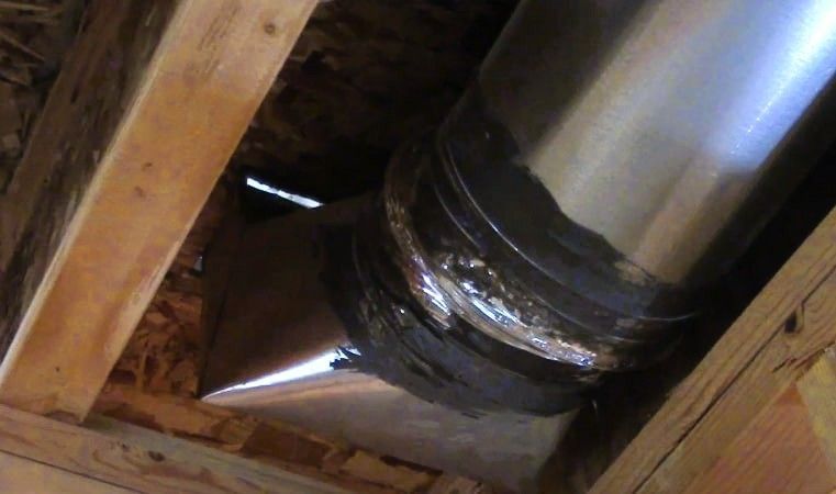 Close-up of a repaired metal duct joint with black sealant in an attic