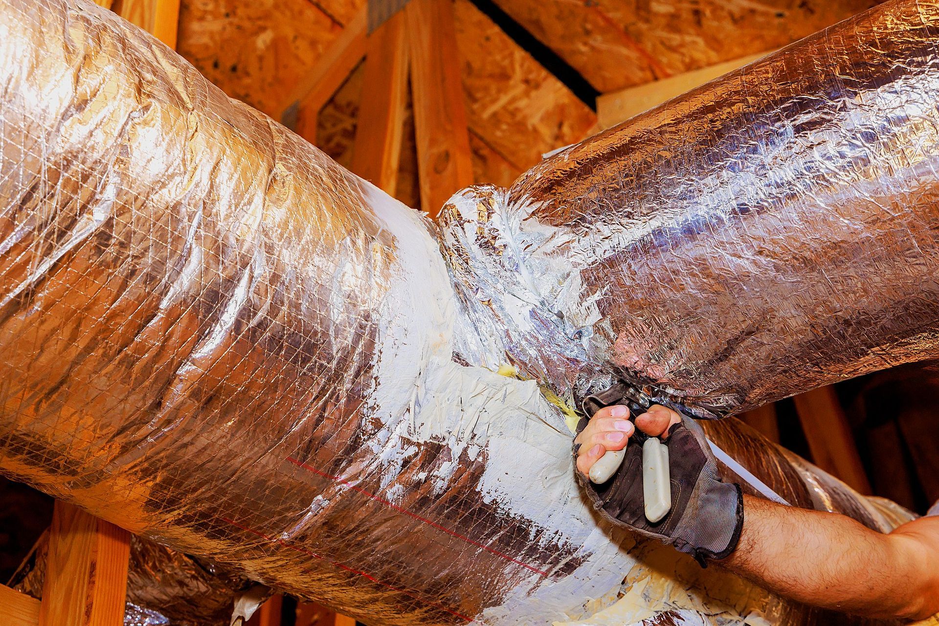 Professional duct sealing technician repairing HVAC air ducts with insulation in attic