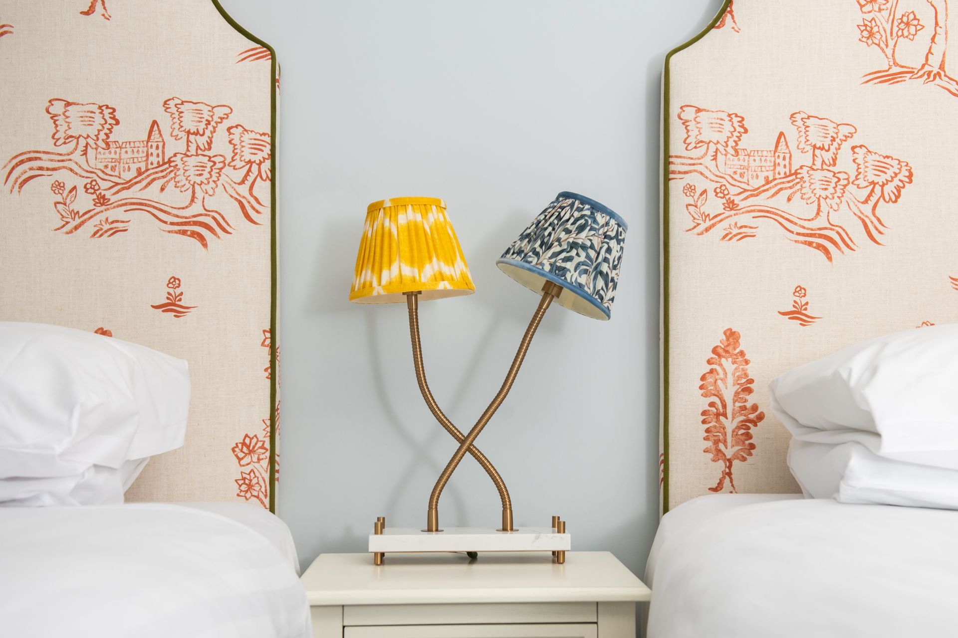 Twin beds with patterned headboards flanking a nightstand with a lamp.