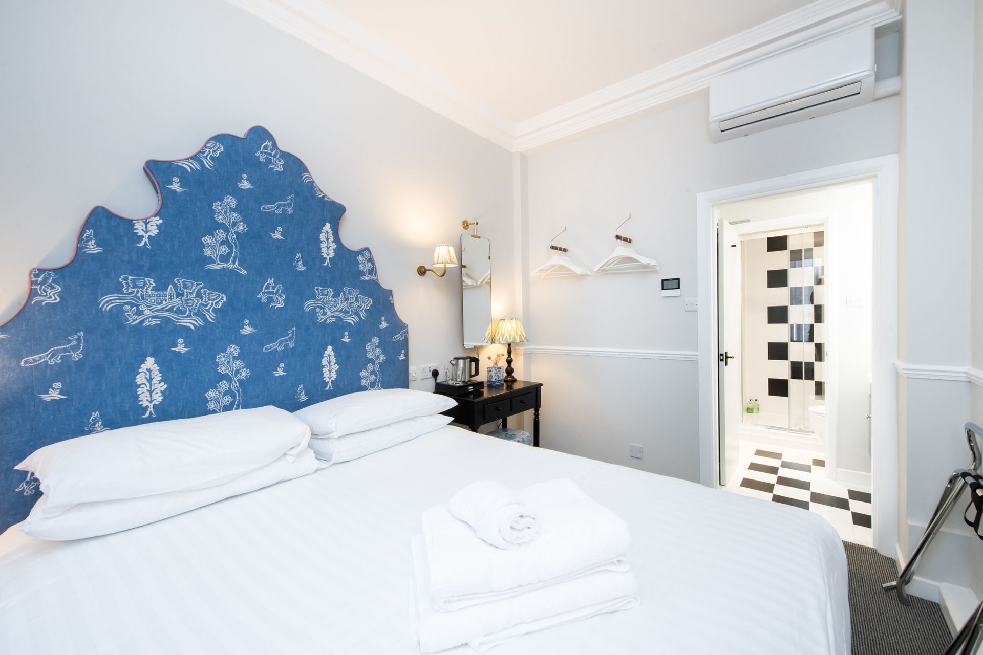 Bedroom with blue patterned headboard, white bedding, and a black and white tiled bathroom visible through an open door.
