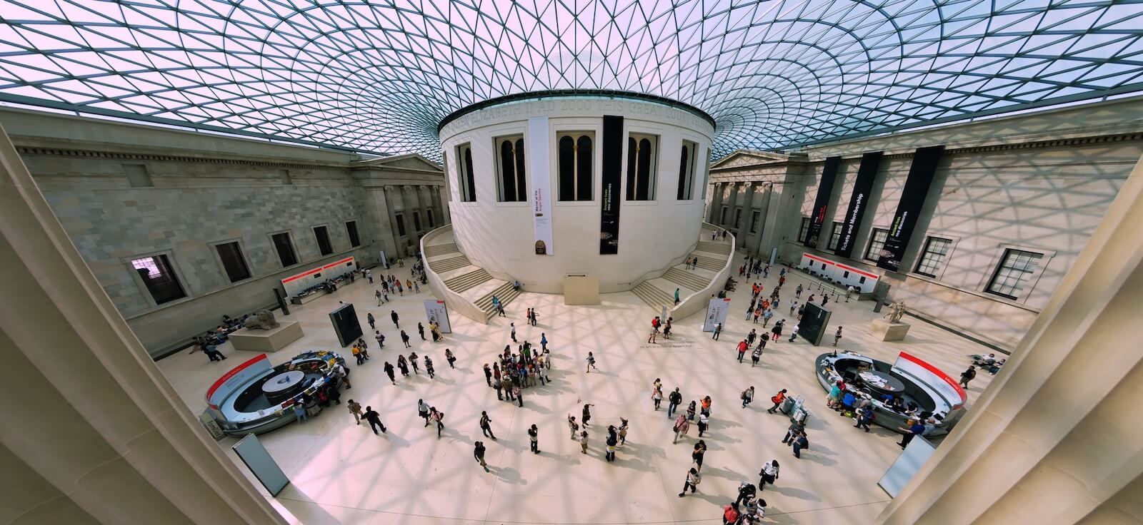 Interior view of the British Museum's Great Court, with people, a large round structure, and glass ceiling.