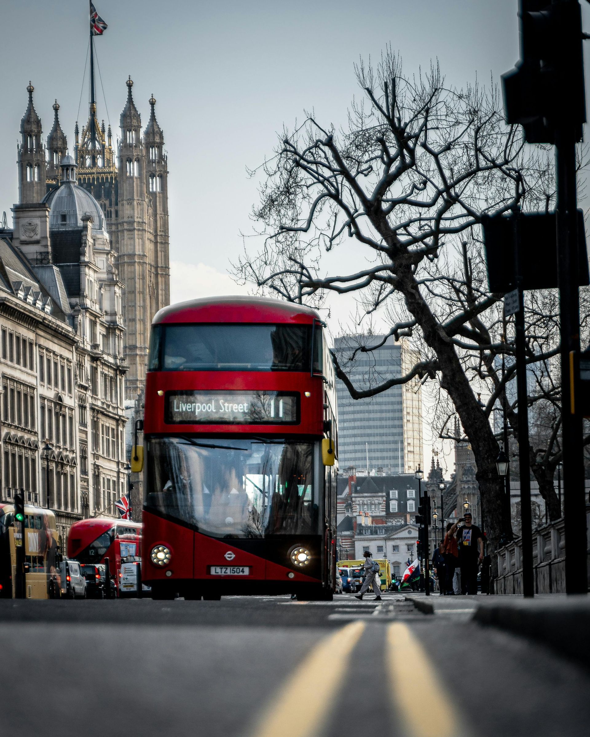Red double-decker bus on a street in London with a view of Big Ben in the background.