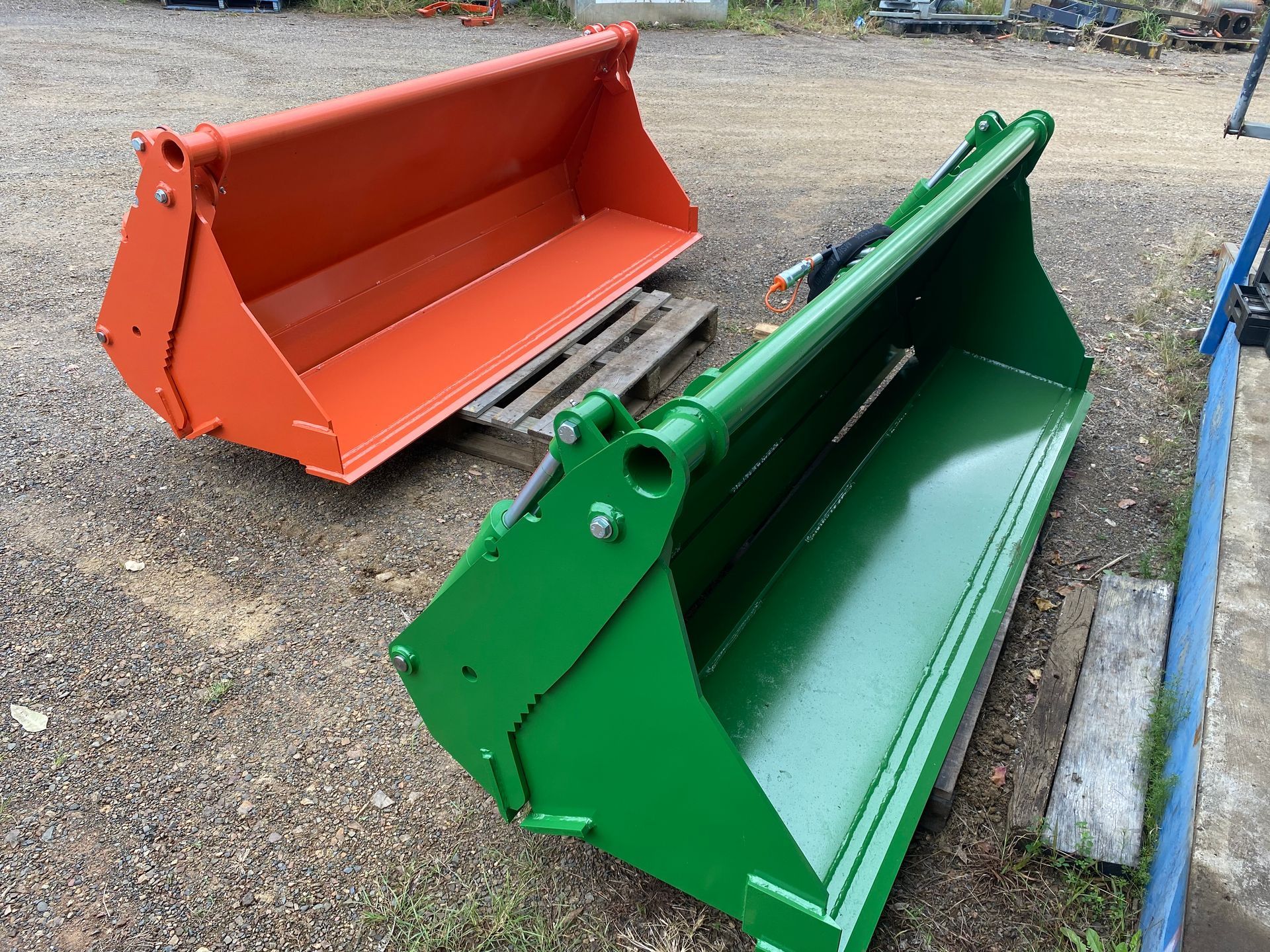 A green and an orange bucket are sitting next to each other on a pallet.— Wingham Farm Machinery in Wingham, NSW