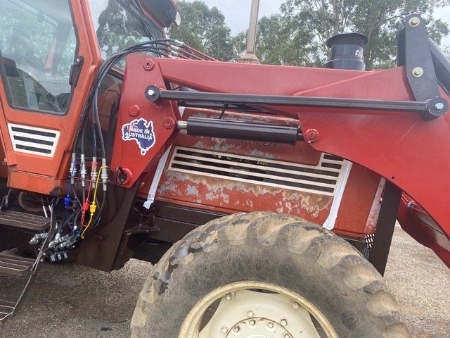 A Red Tractor With a Large Tire is Parked in a Dirt Field — Wingham Farm Machinery In Wingham, NSW