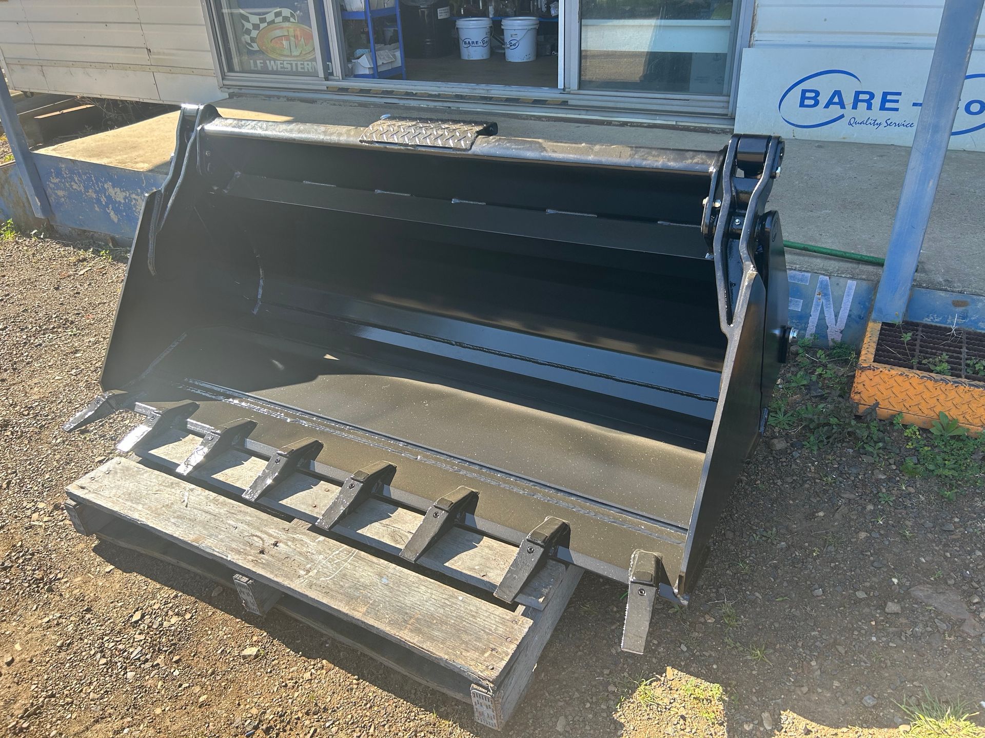 A large metal bucket is sitting on top of a wooden pallet.— Wingham Farm Machinery in Wingham, NSW