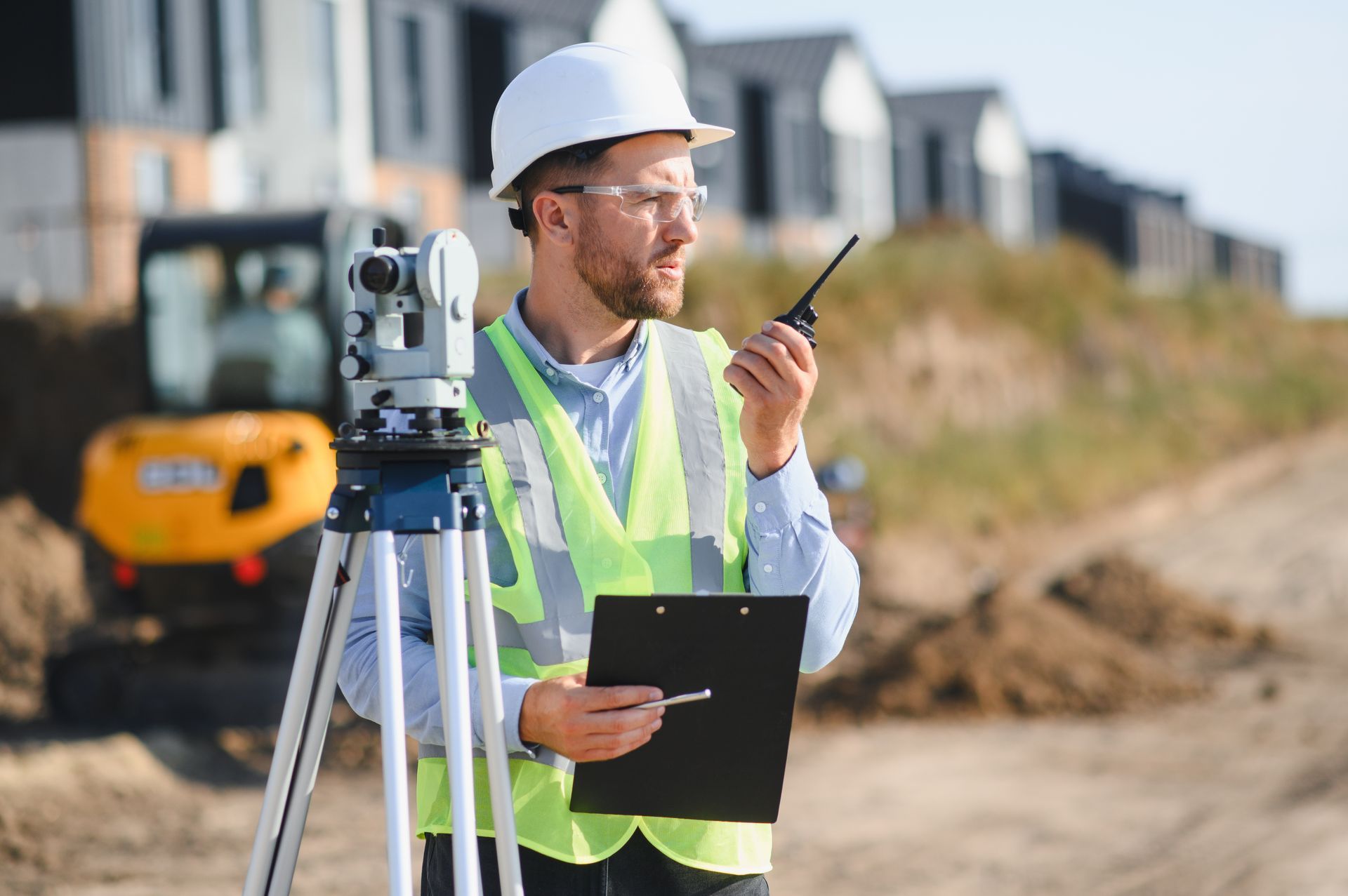 Man in hard hat and safety vest using a tripod for residential land surveying services.