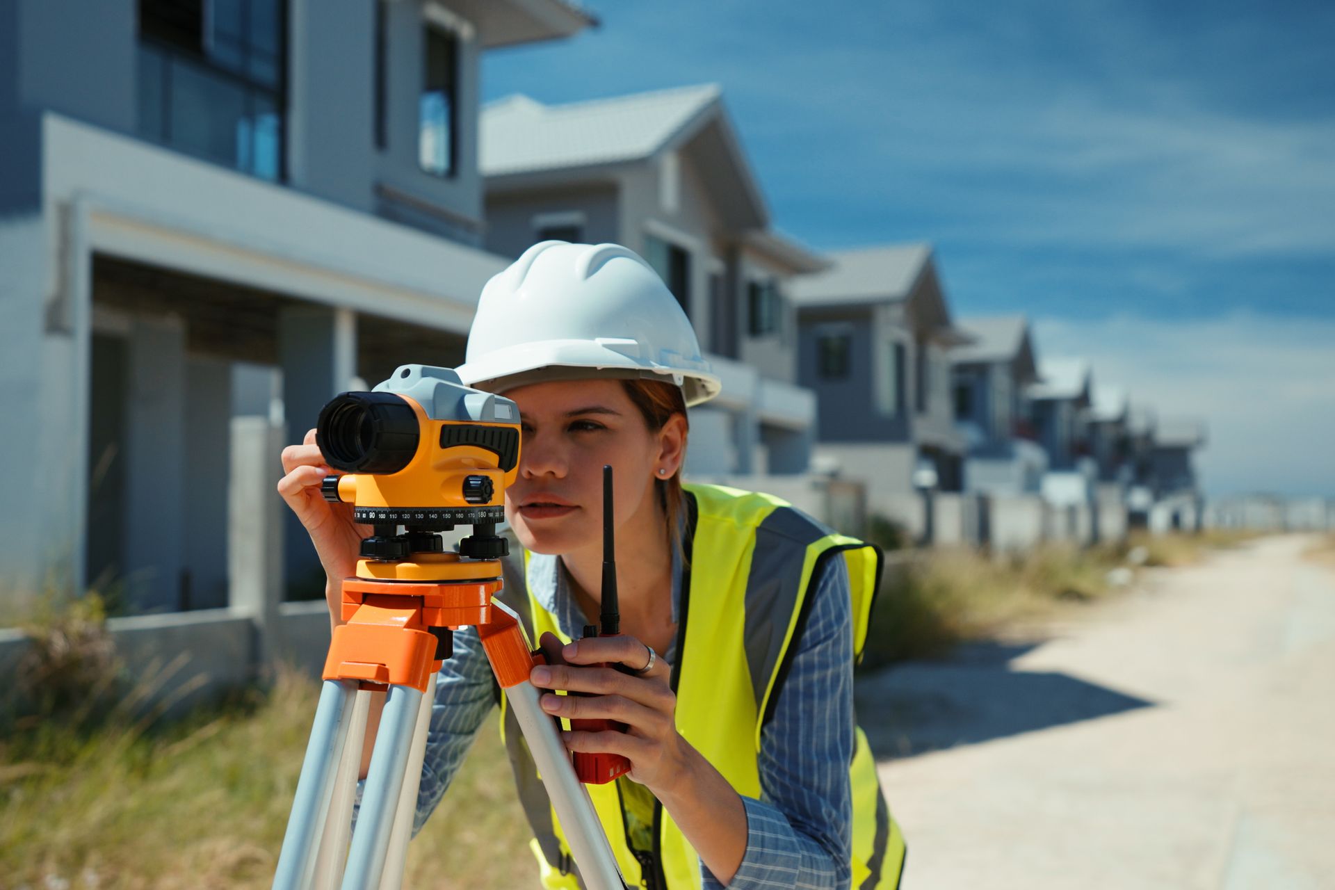 A female surveyor is using a theodolite to measure the land at a residence.