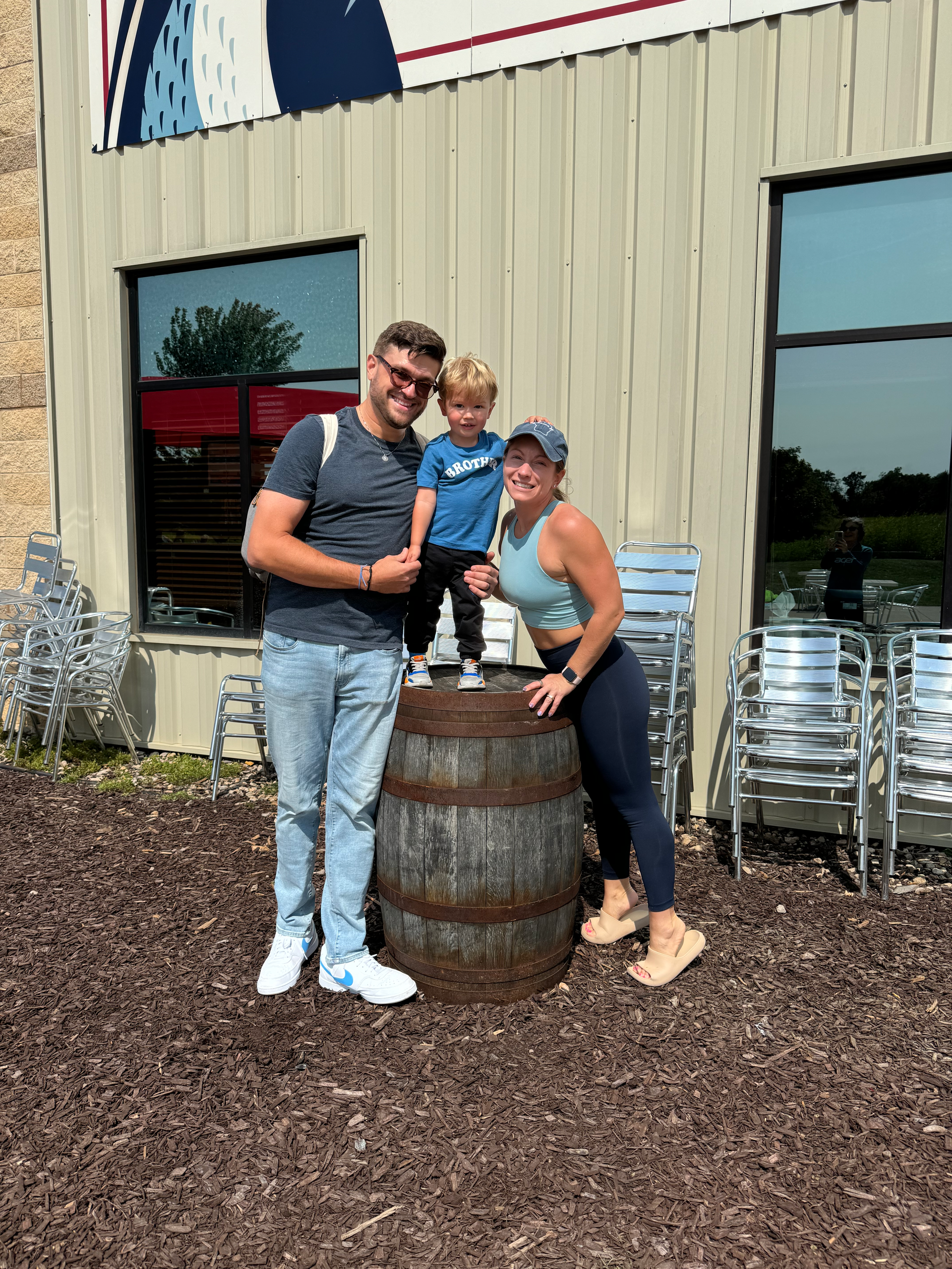 A man, woman, and toddler are standing next to a barrel in front of a building.