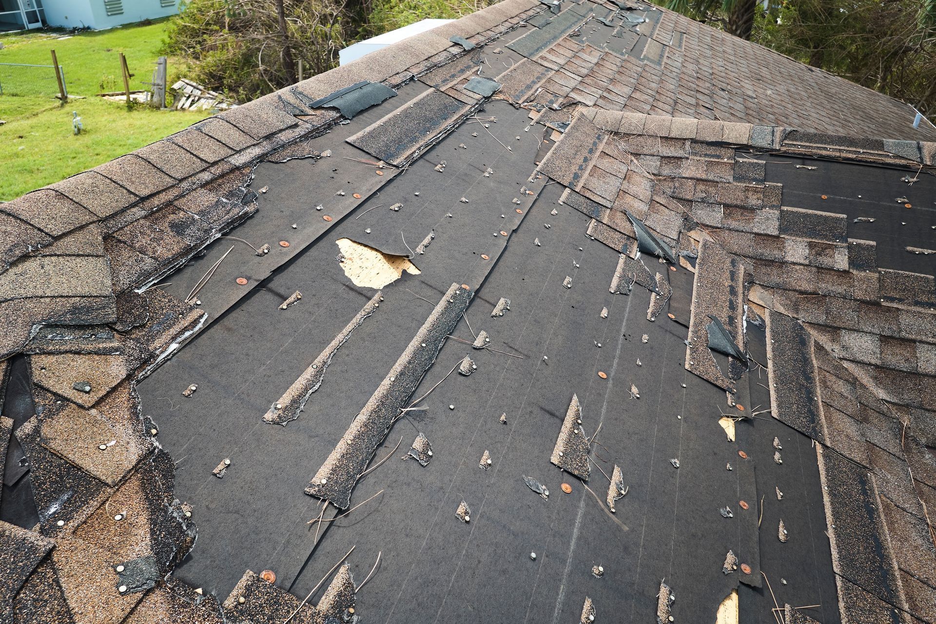 Damaged shingle roof with missing sections and exposed underlayment near the ridge