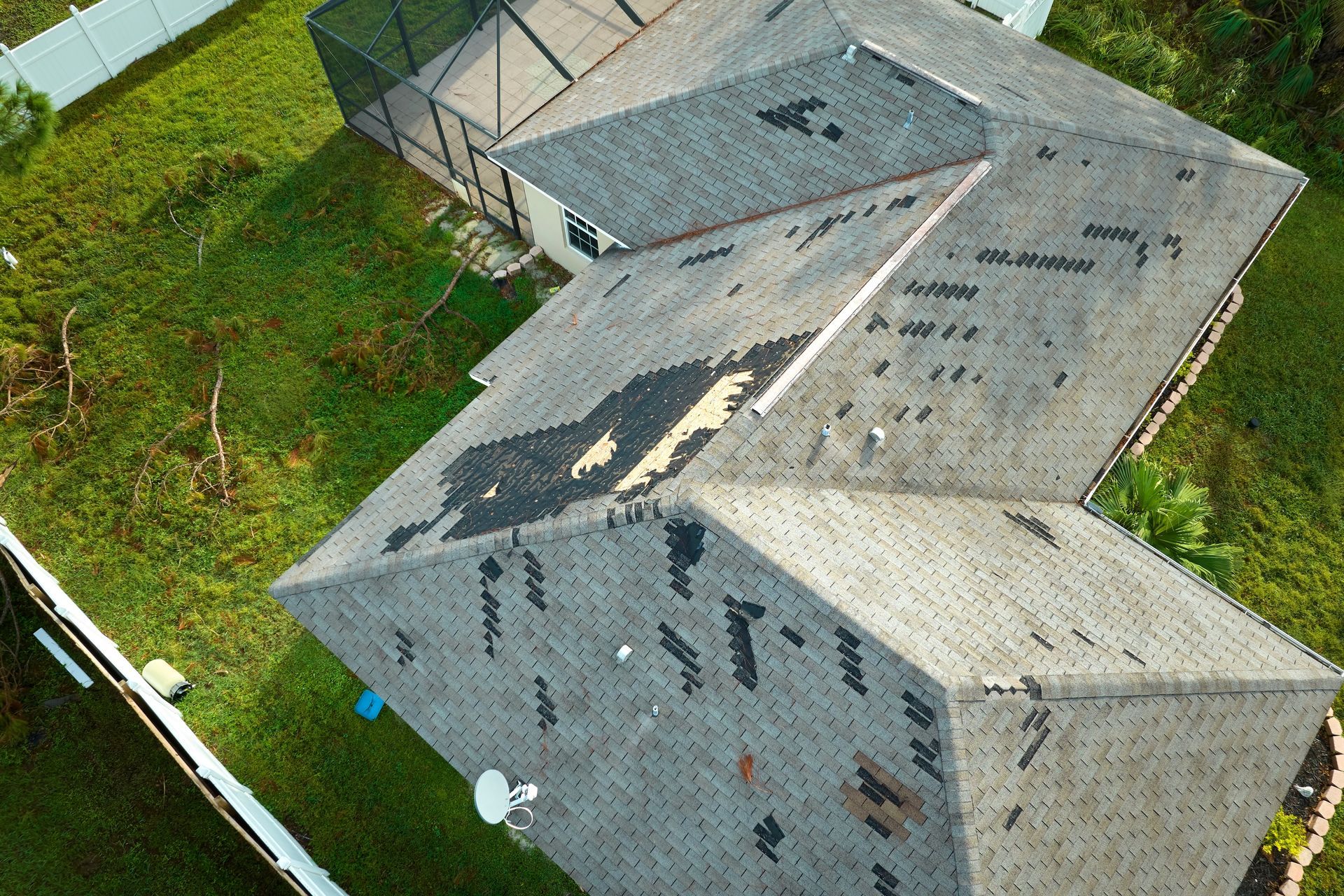 Aerial view of a gray shingled house roof with roof damage and a yard below.