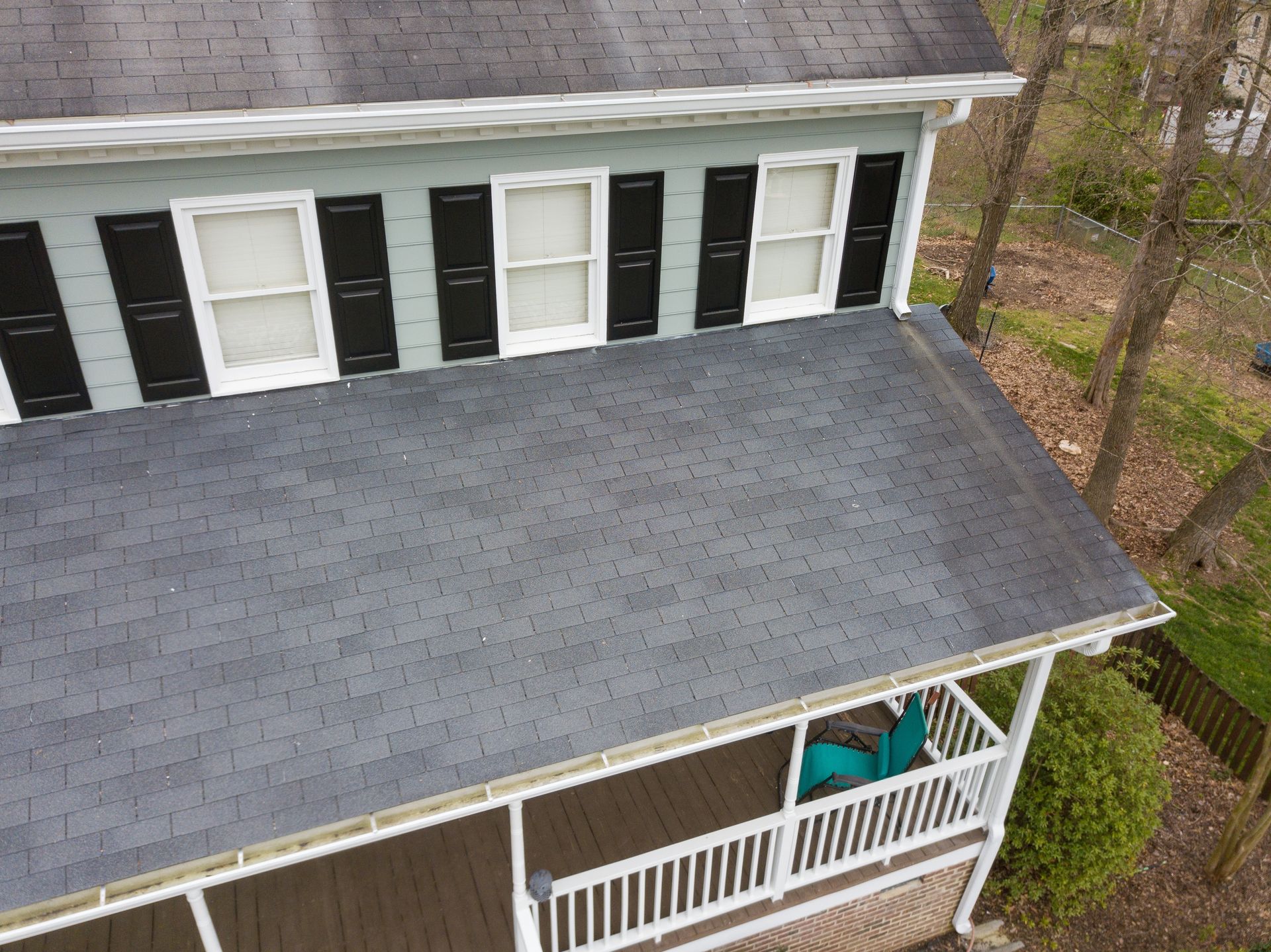 Aerial view of a gray-roofed house with black shutters and a white porch