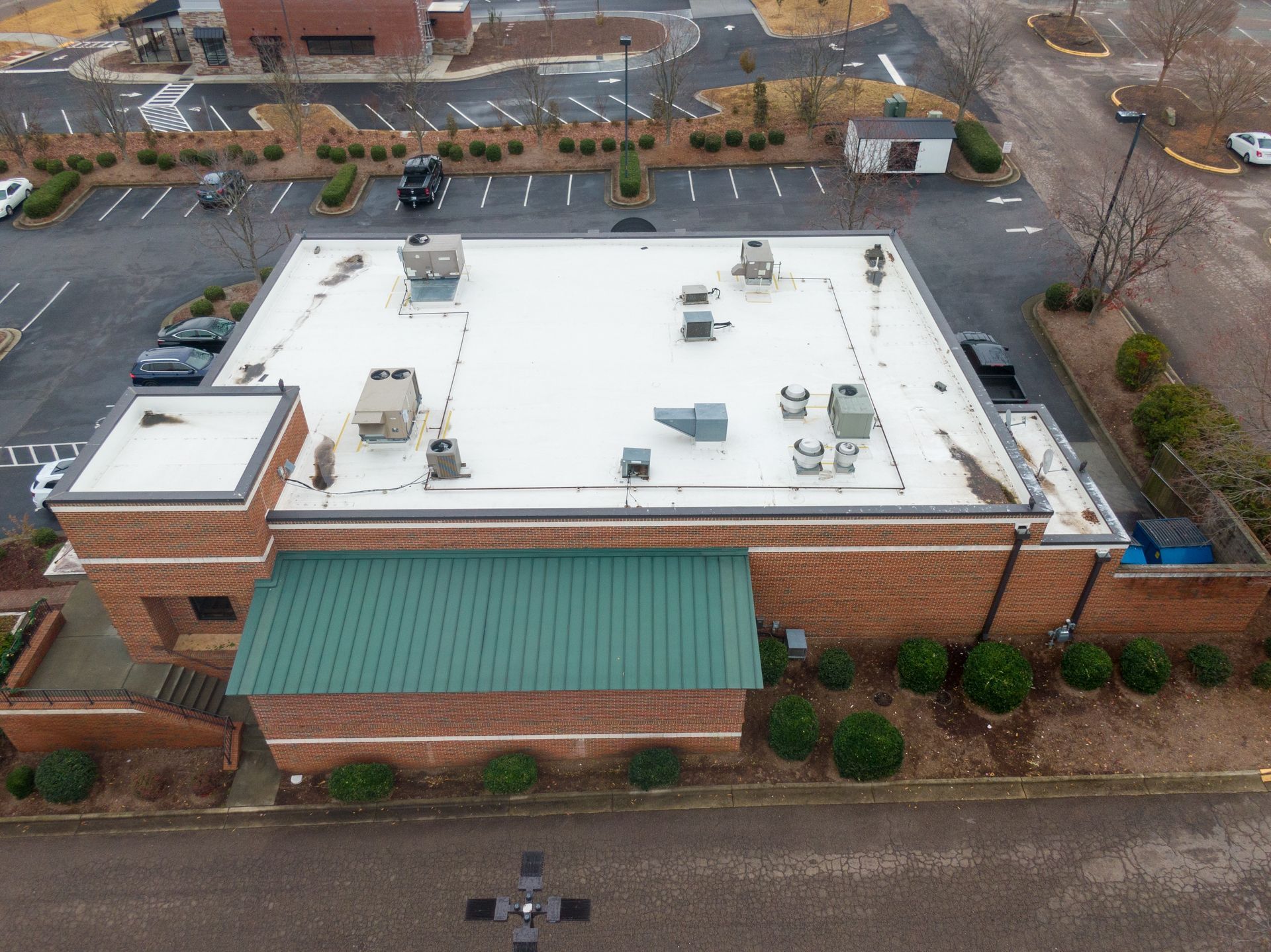 Aerial view of a brick building with a white rooftop and green awning beside a parking lot