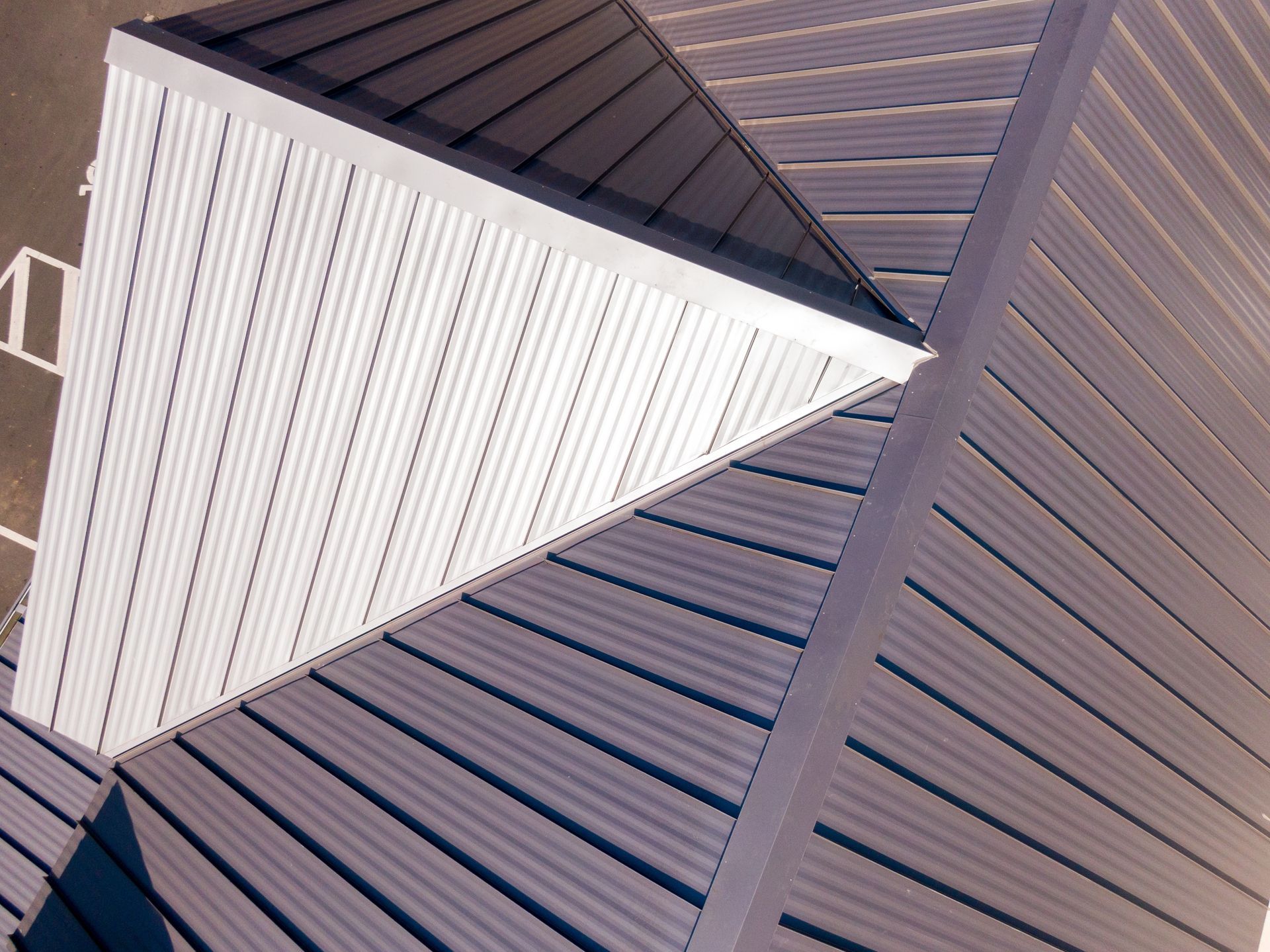 Aerial view of a triangular white-roofed structure beside a brown-striped roof.