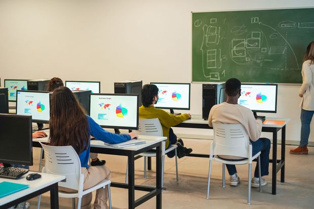 a group of people are sitting at desks in front of computer monitors in a classroom | Apple Security Solutions