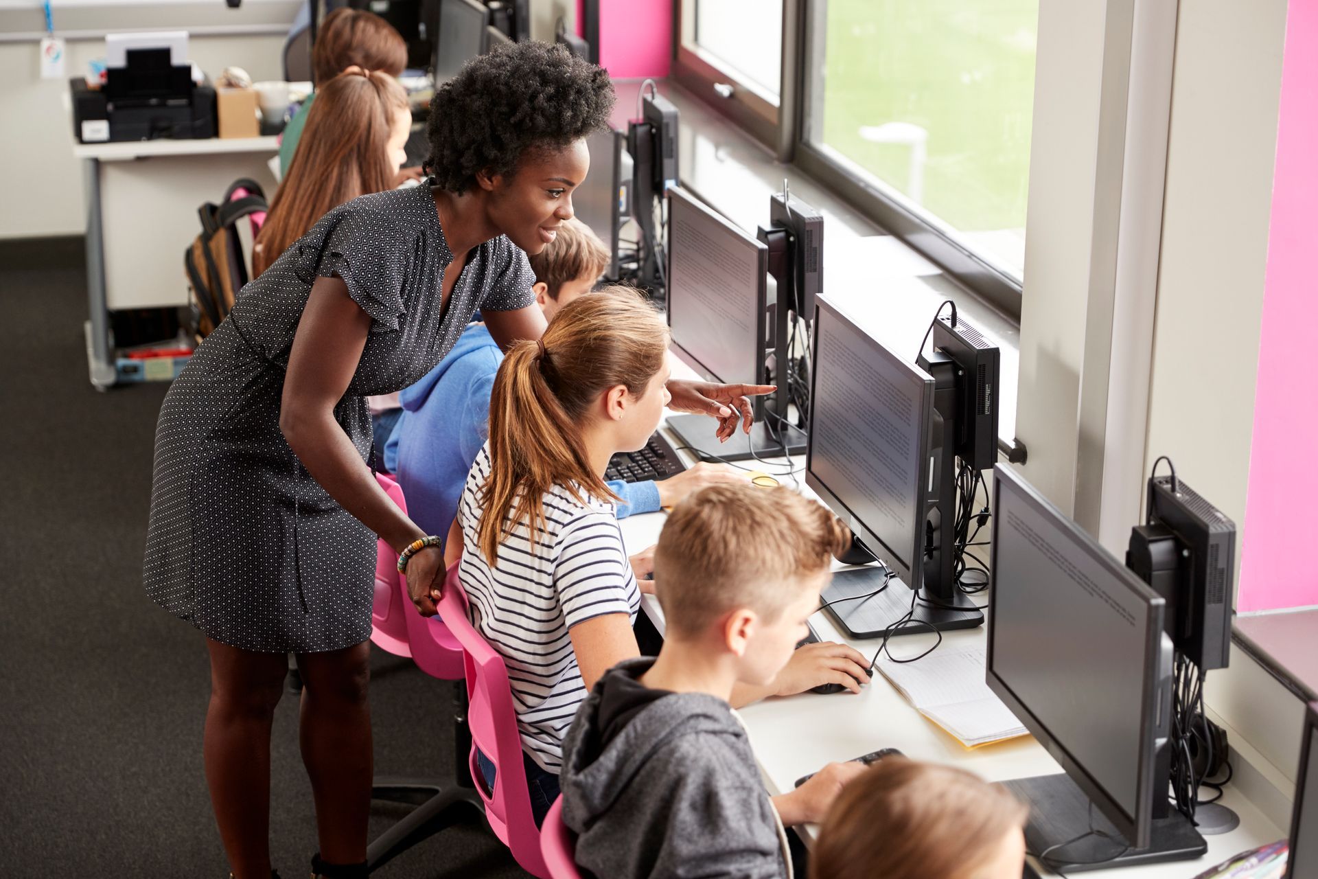 a teacher is teaching a group of children how to use computers in a classroom | Apple Security Solutions