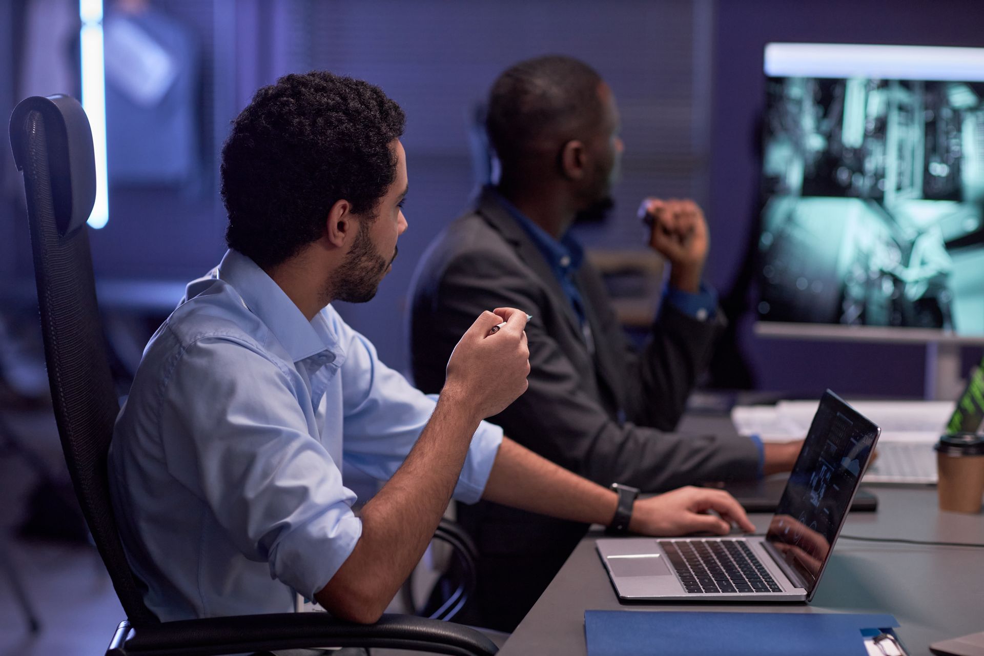 two men are sitting at a table with laptops | Apple Business Security