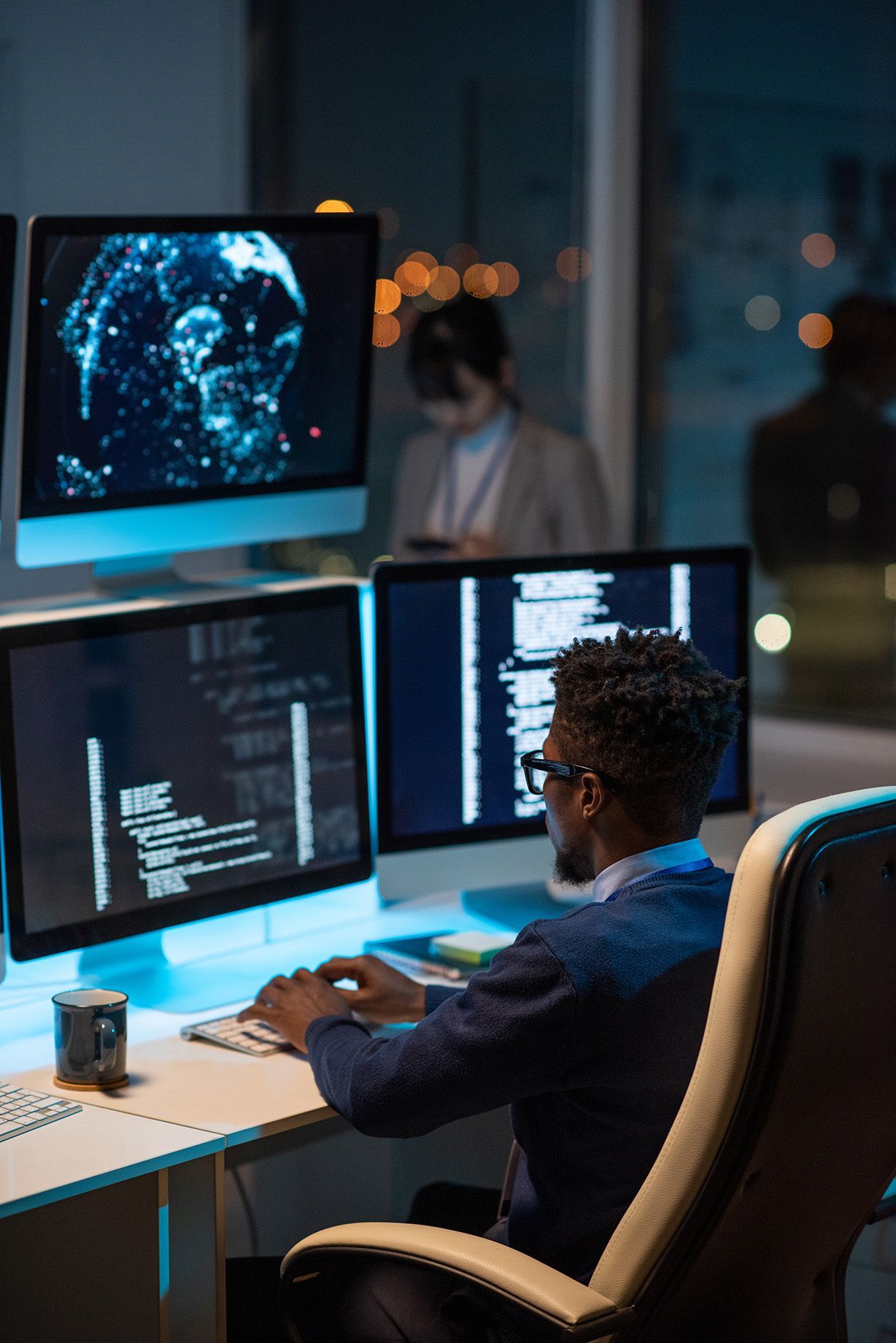 a man is sitting at a desk in front of three computer monitors | Apple Business Security