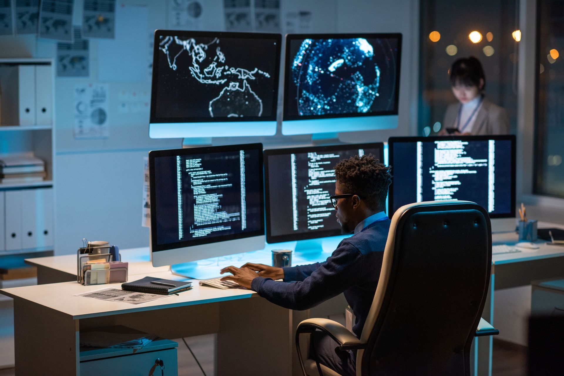 a man is sitting at a desk in front of three computer monitors | Apple Business Security