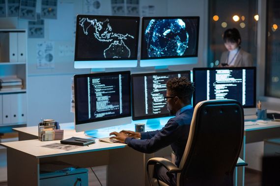 a man is sitting at a desk in front of three computer monitors | Apple Security Solutions