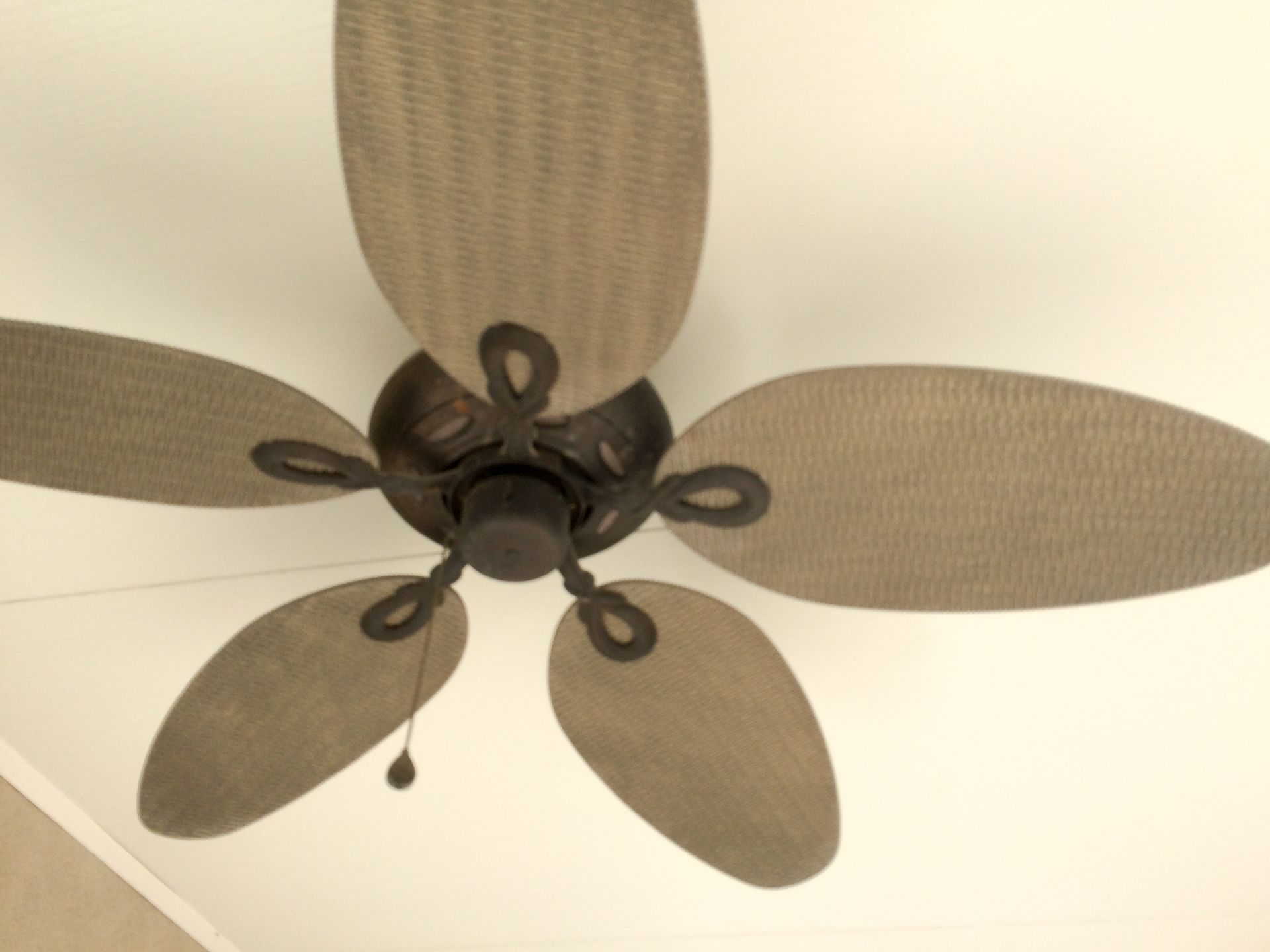 Ceiling fan on white background overhead with big leaf blades.