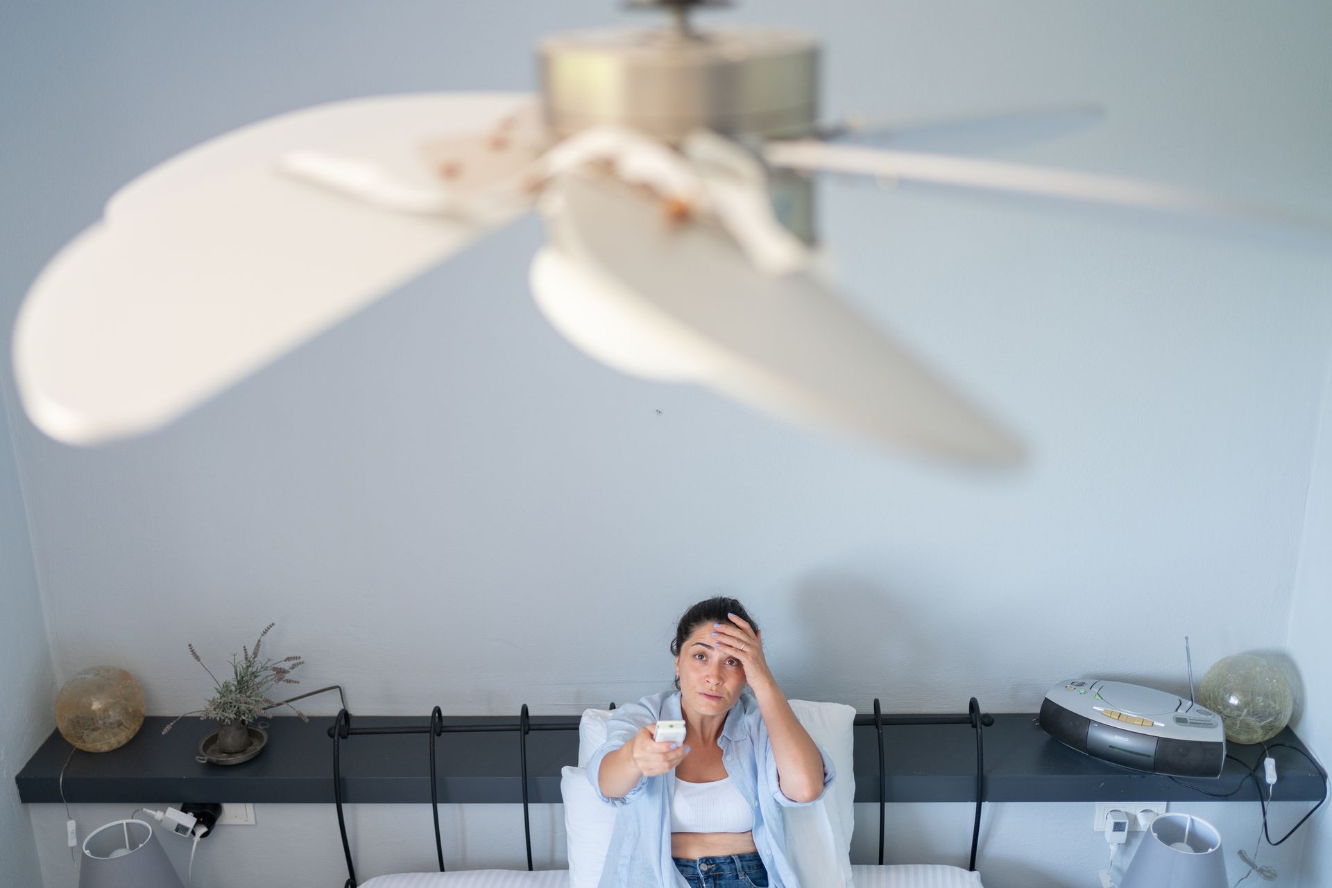 Woman using a remote control to turn on a ceiling fan.