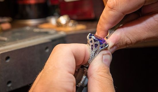 Un gioielliere durante una  lavorazione di un anello di con una  pietra blu e dei brillanti 