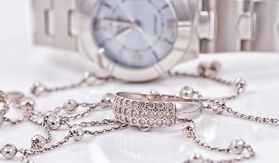Un anello con dei brillantini, una catena d’ oro rosa e un orologio su uno sfondo bianco 