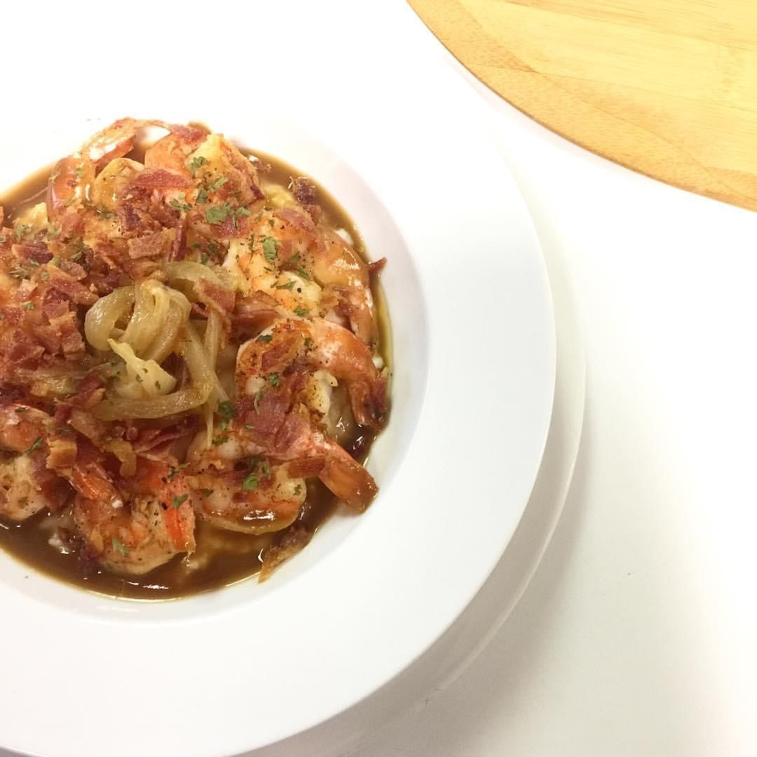 Shrimp and bacon pasta in a white bowl with a wooden cutting board in the background.