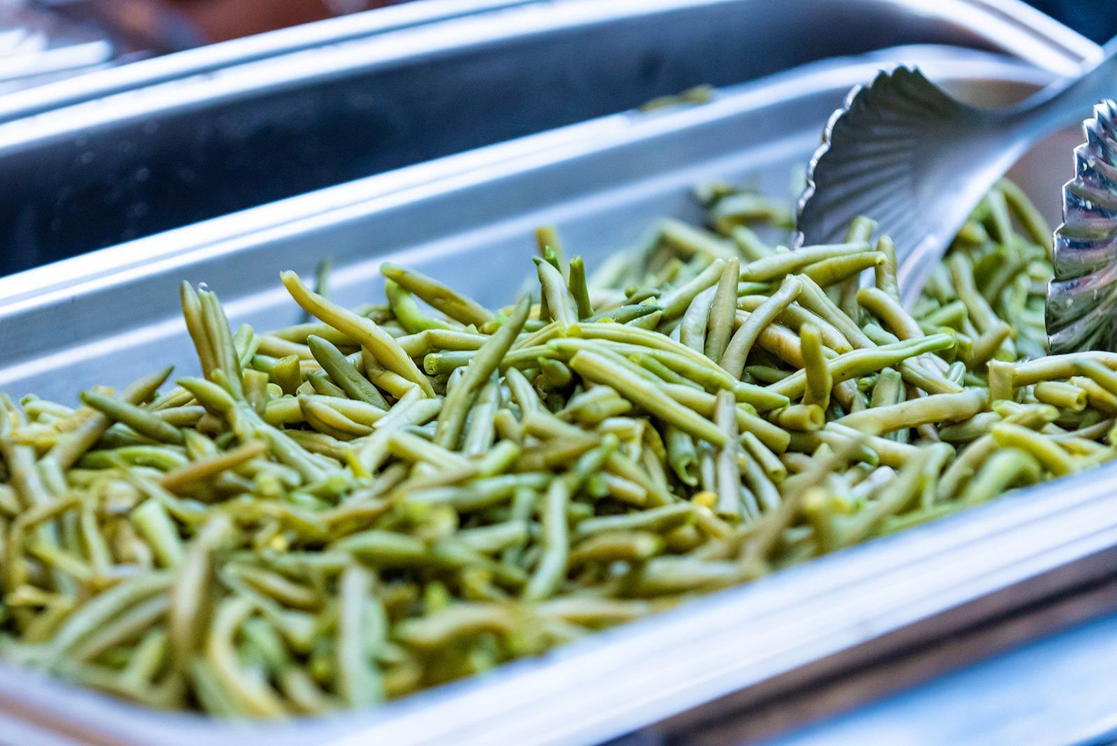 Green beans in a silver buffet serving dish, with tongs.