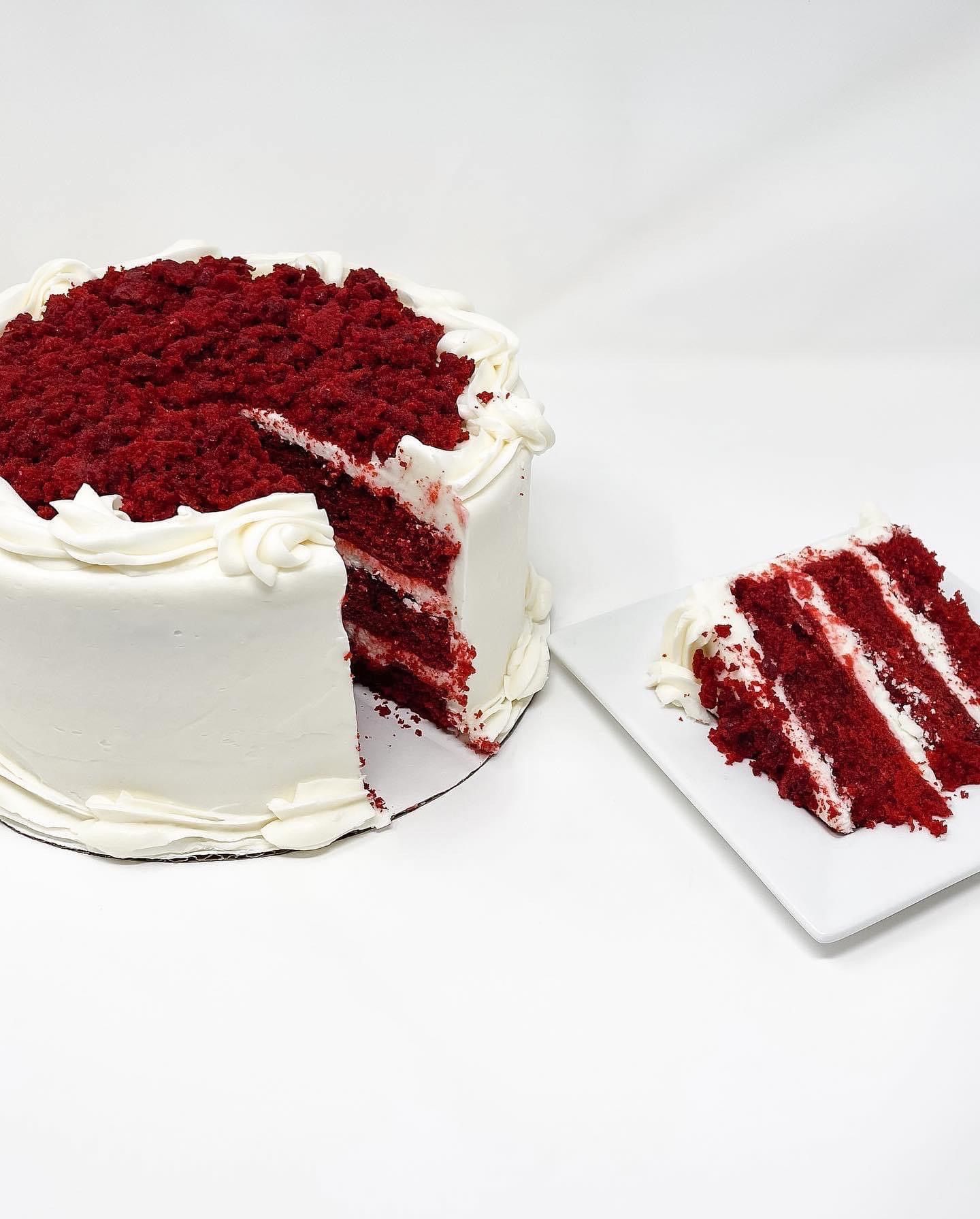 Red velvet cake with white frosting, sliced to show layers and a piece on a plate.