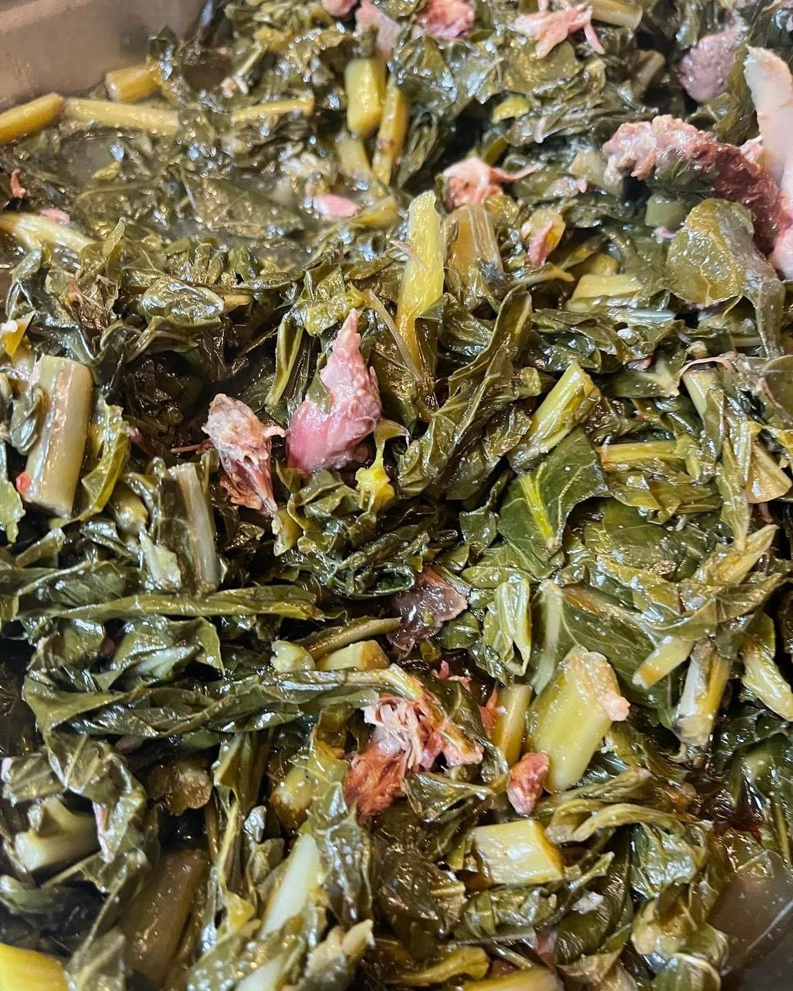 Collard greens cooked with ham, a Southern dish. Dark green leaves and stems with pink ham pieces are visible.