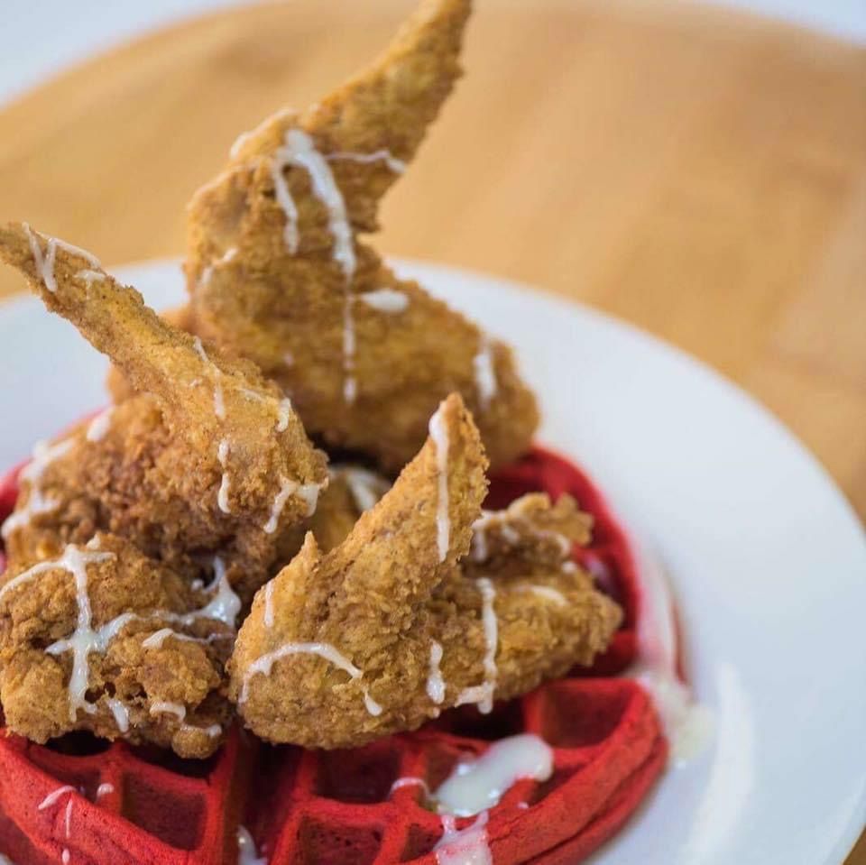 Fried chicken wings drizzled with sauce sit atop a red waffle on a white plate.