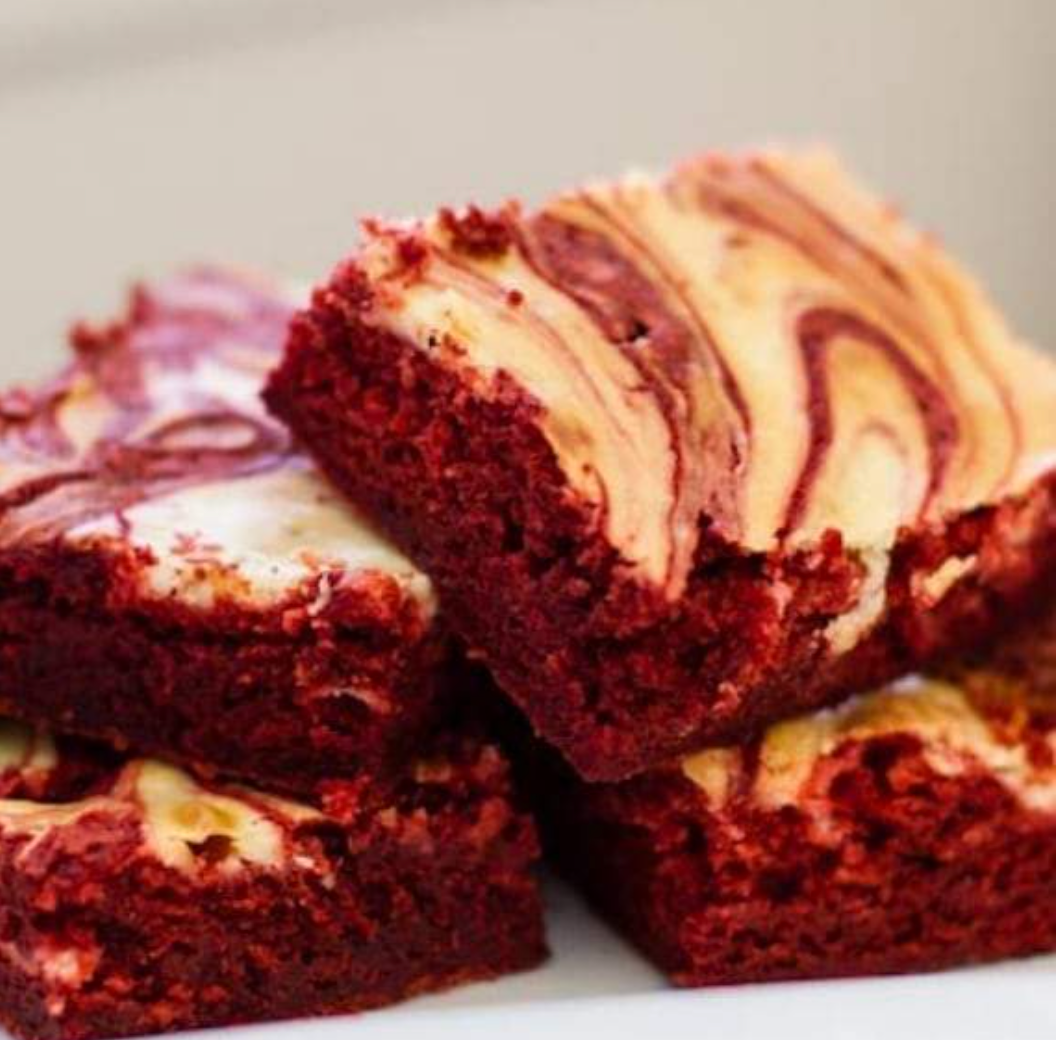 Red velvet brownies with swirled cream cheese frosting, stacked on a white surface.
