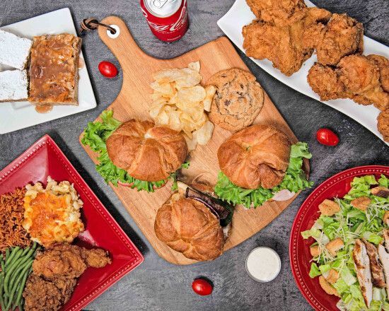 Assorted fast food items: fried chicken, sandwiches, salad, sides, cookies, and a soda arranged on a dark surface.