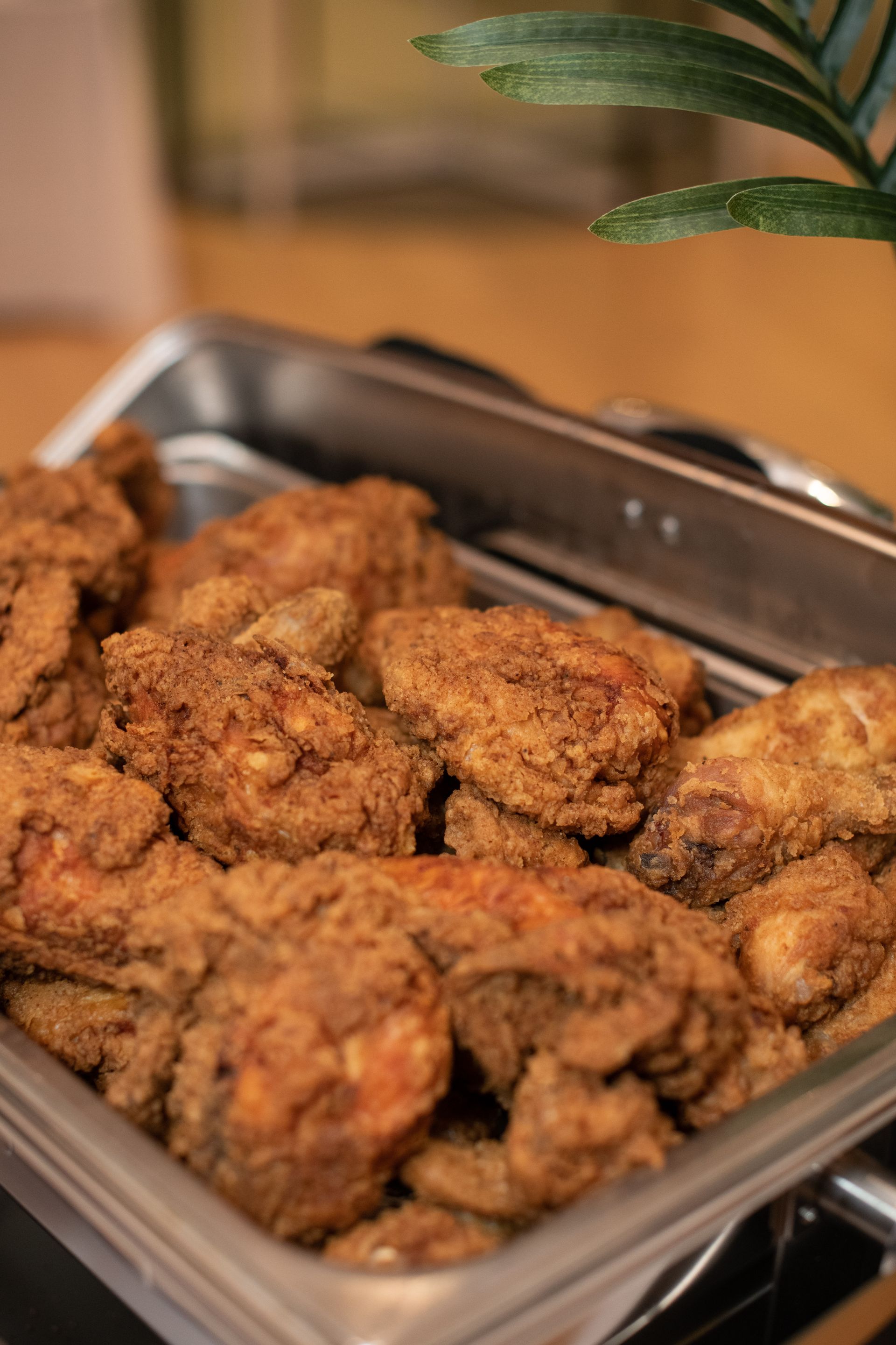 A metal tray filled with crispy, golden-brown fried chicken pieces. A pair of tongs rests on the side.