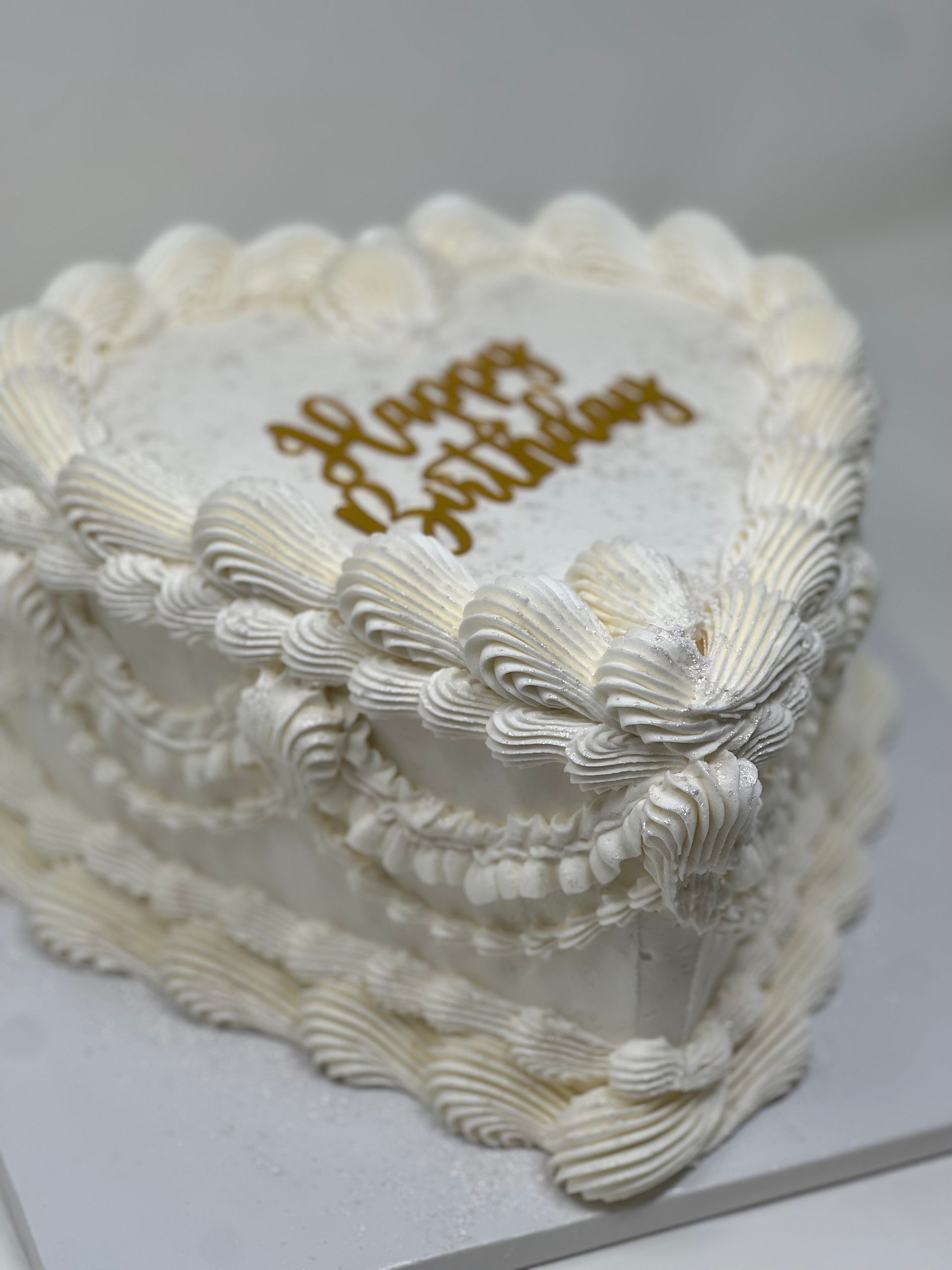 Heart-shaped cake with white frosting and piped decorative edges. Gold 