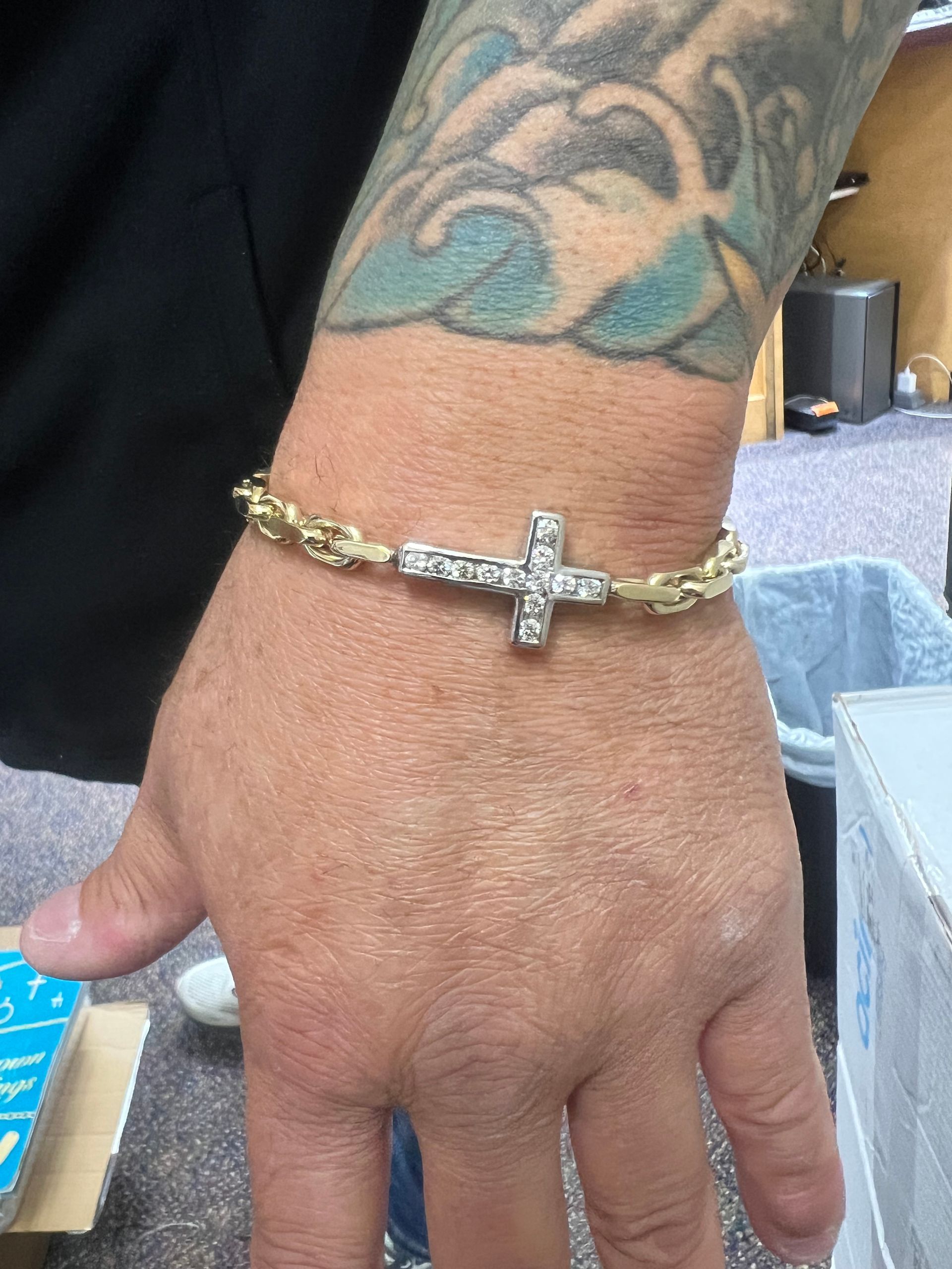 A person with a tattoo on their arm is wearing a bracelet with a cross on it