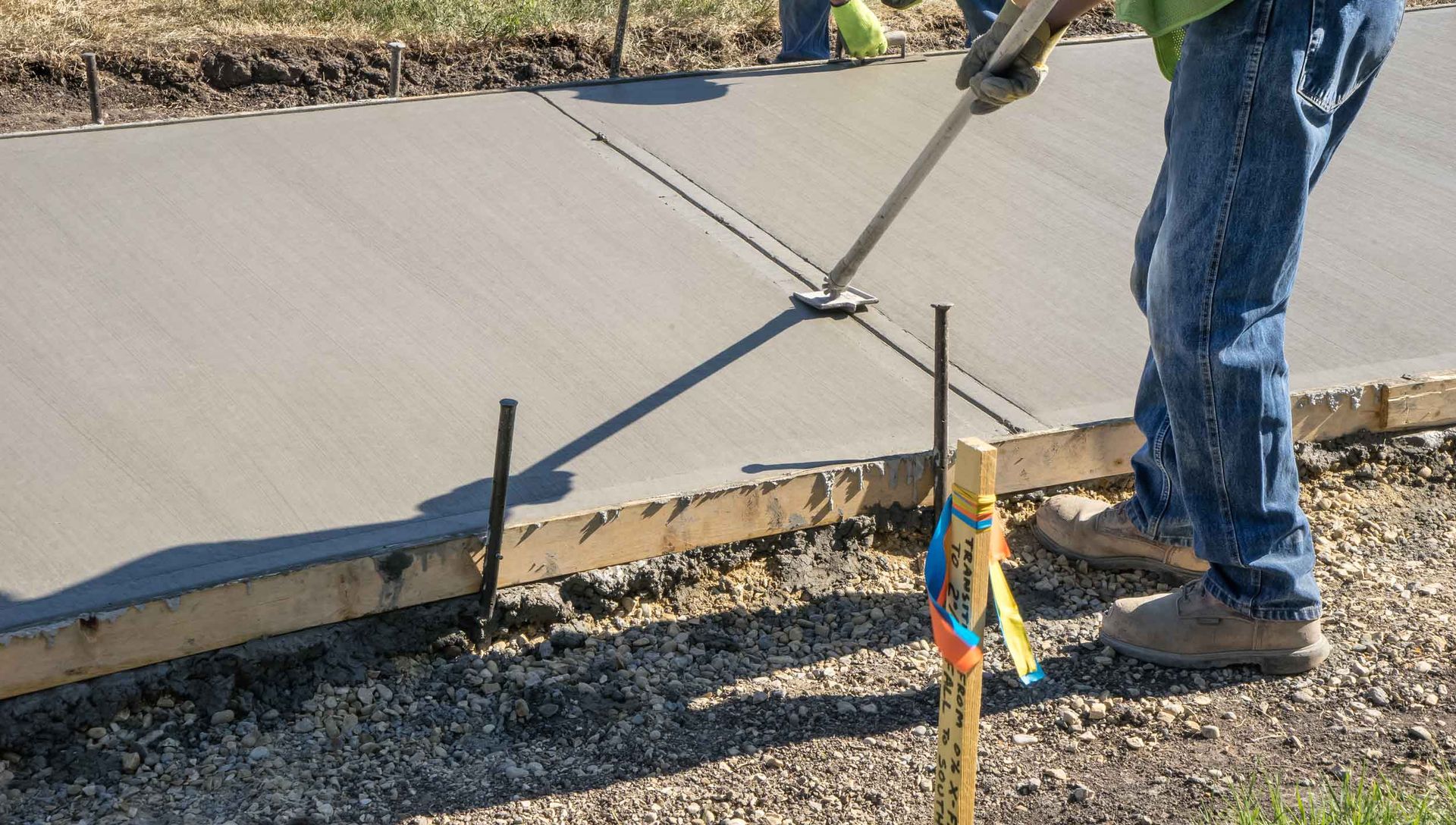 Worker smoothing wet concrete sidewalk with a tool, outdoors.