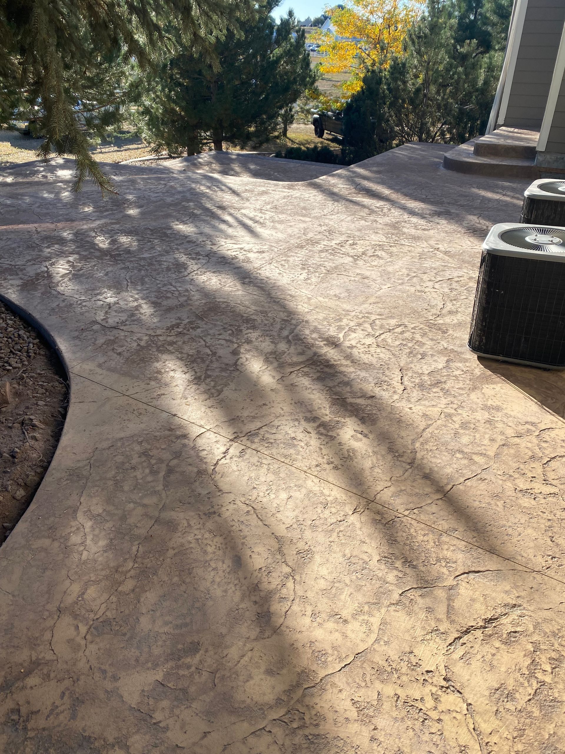 Four black Adirondack chairs surrounding a square, wooden coffee table with a plant, on a concrete patio.