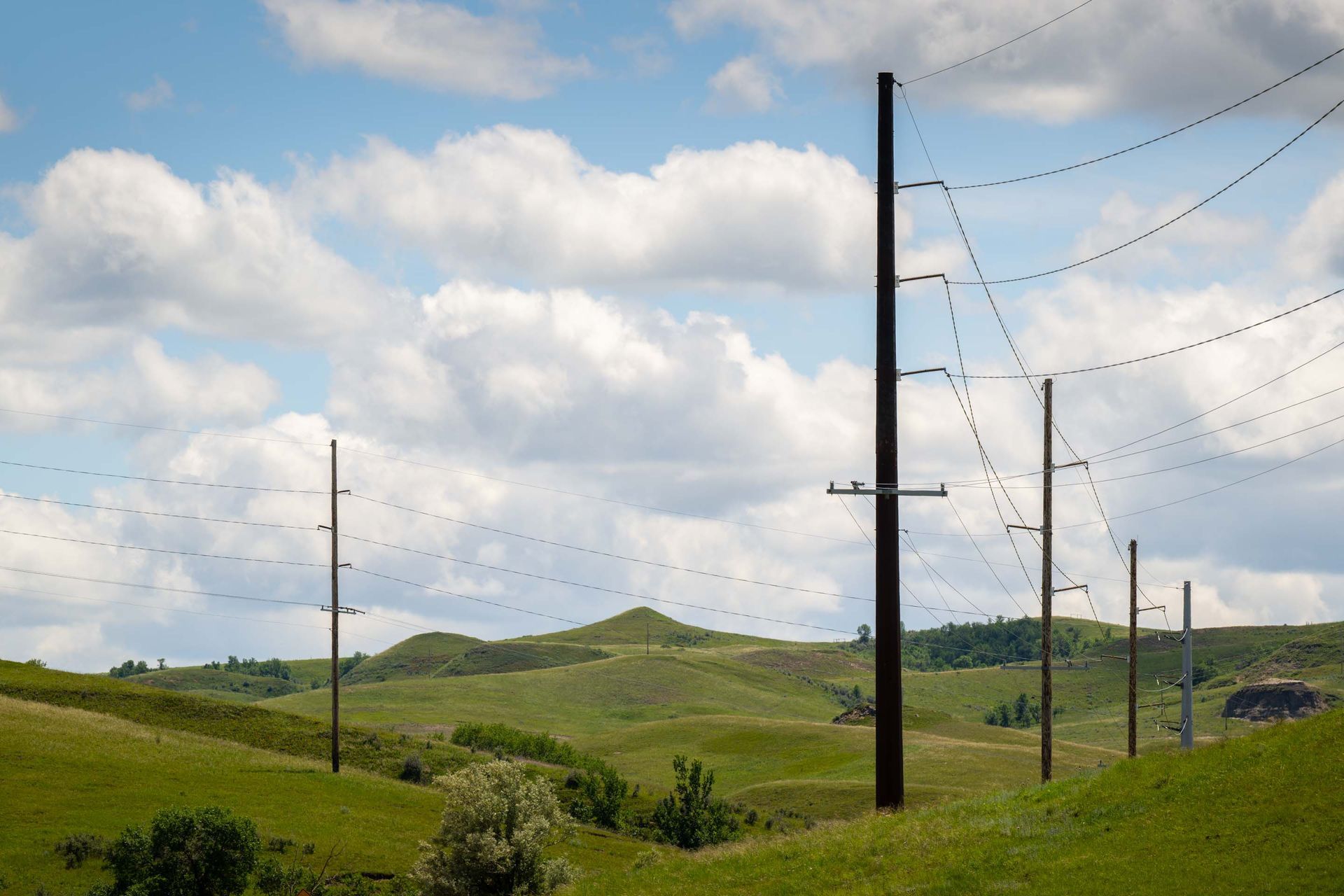 Green hills with power lines under a cloudy blue sky.