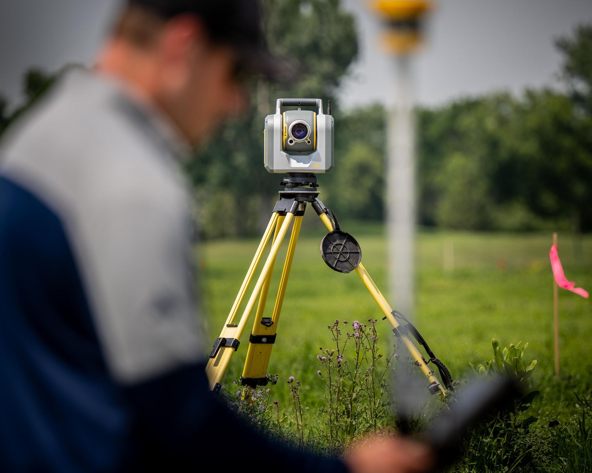 Surveyor using a total station on a tripod in a grassy field.
