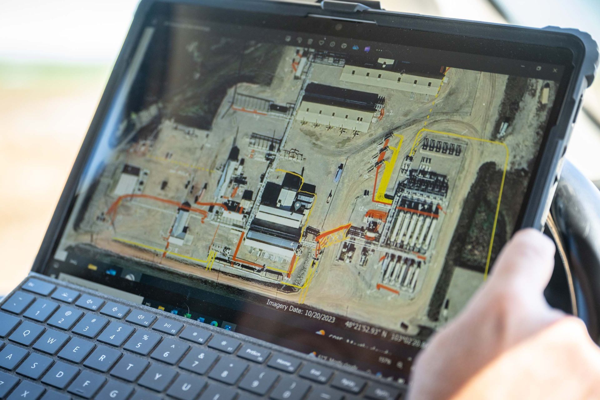 Tablet displaying a map overlay of an industrial site; a hand is pointing at the screen.
