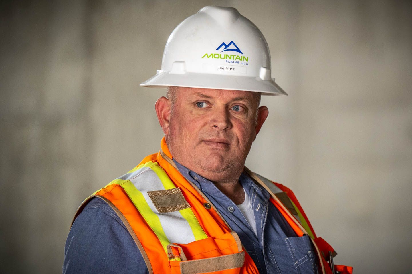 Construction worker wearing a white hard hat and orange safety vest, looking to the side.