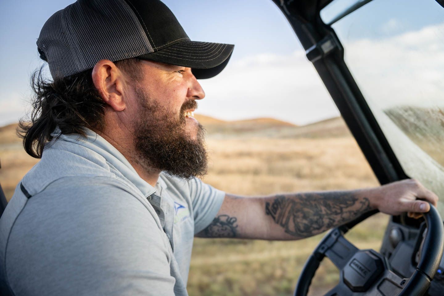 Man driving an off-road vehicle with a smile, wearing a hat, in a field.