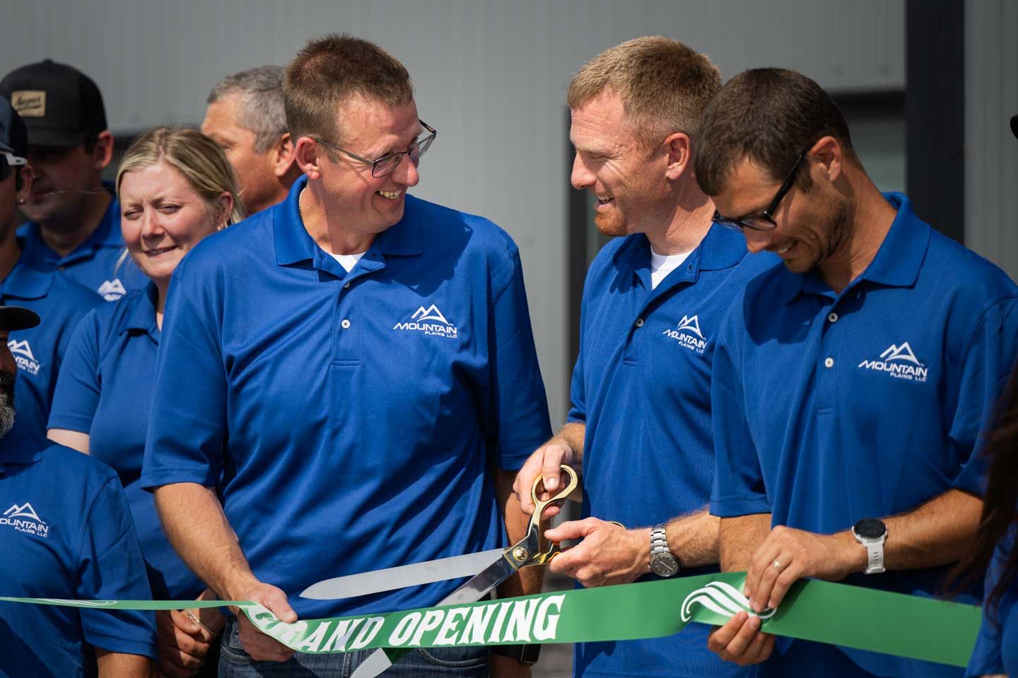 People cutting a ribbon at a grand opening. The ribbon is green and held by people wearing blue shirts.