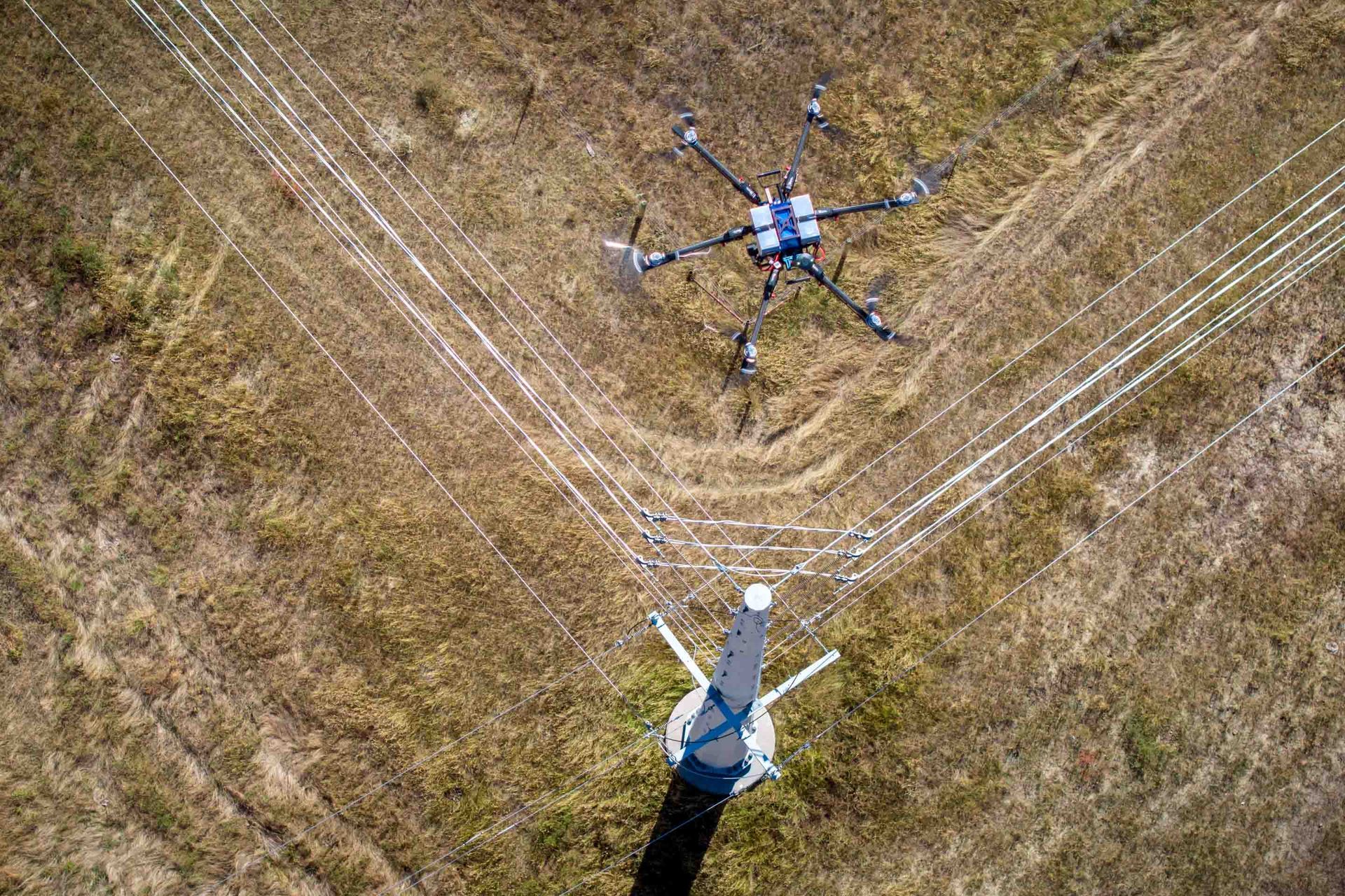 Drone inspecting power lines in a field.  Top-down view with lines and a tower visible.