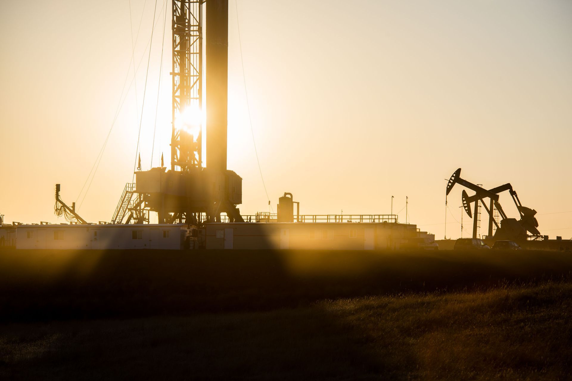 Oil rig silhouetted against a golden sunset, with pump jacks in the background.